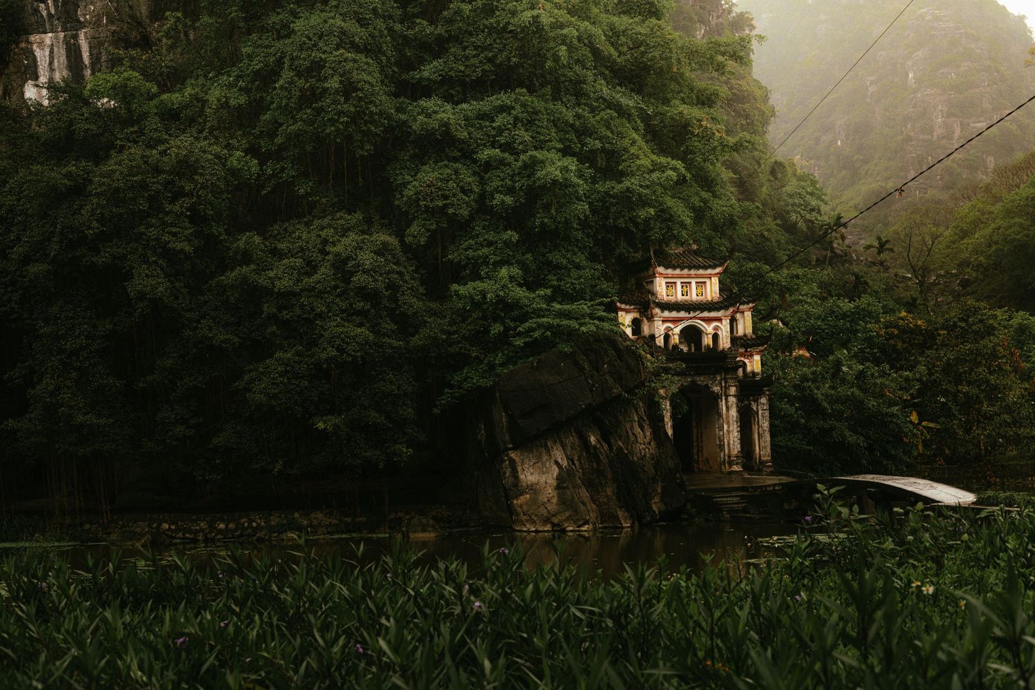 Ancient pagoda tower perched above a lake surrounded by misty mountains and dense vegetation.