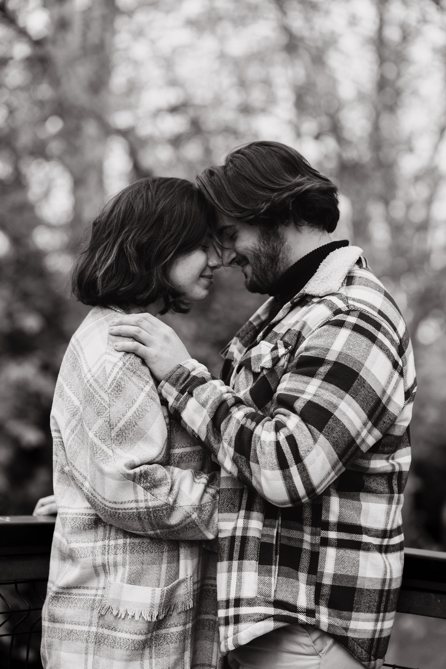 Intimate black and white photo of couple in plaid jackets embracing outdoors.