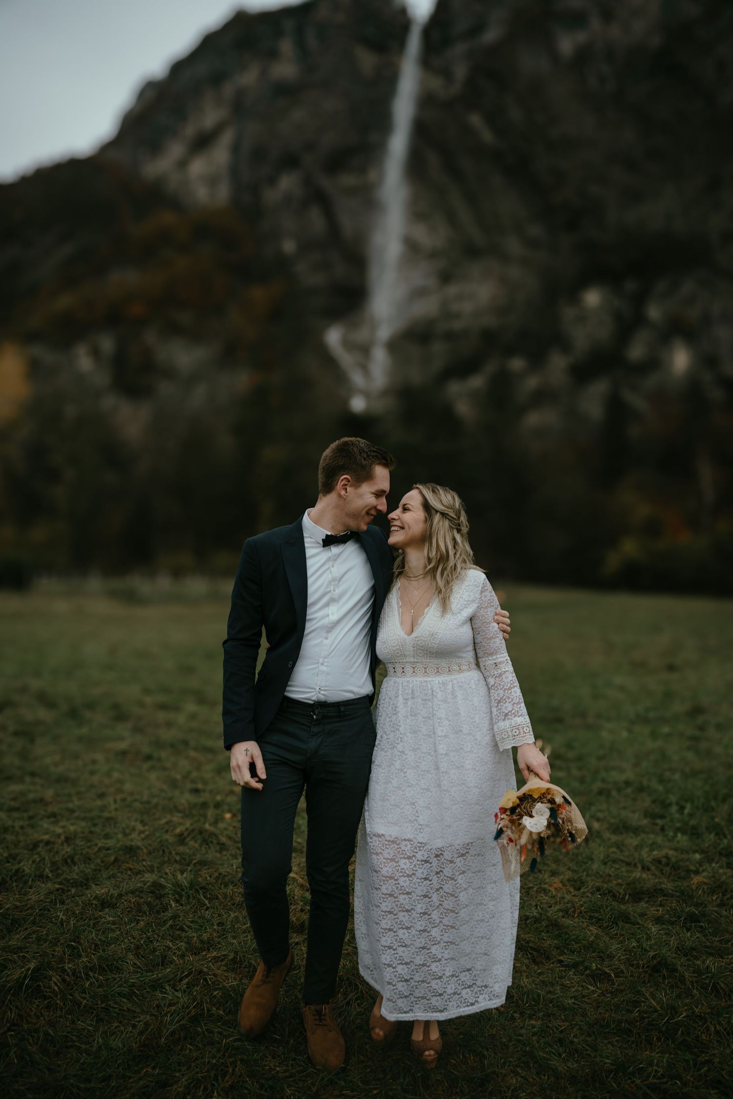 Romantic couple in wedding attire standing before a majestic waterfall.