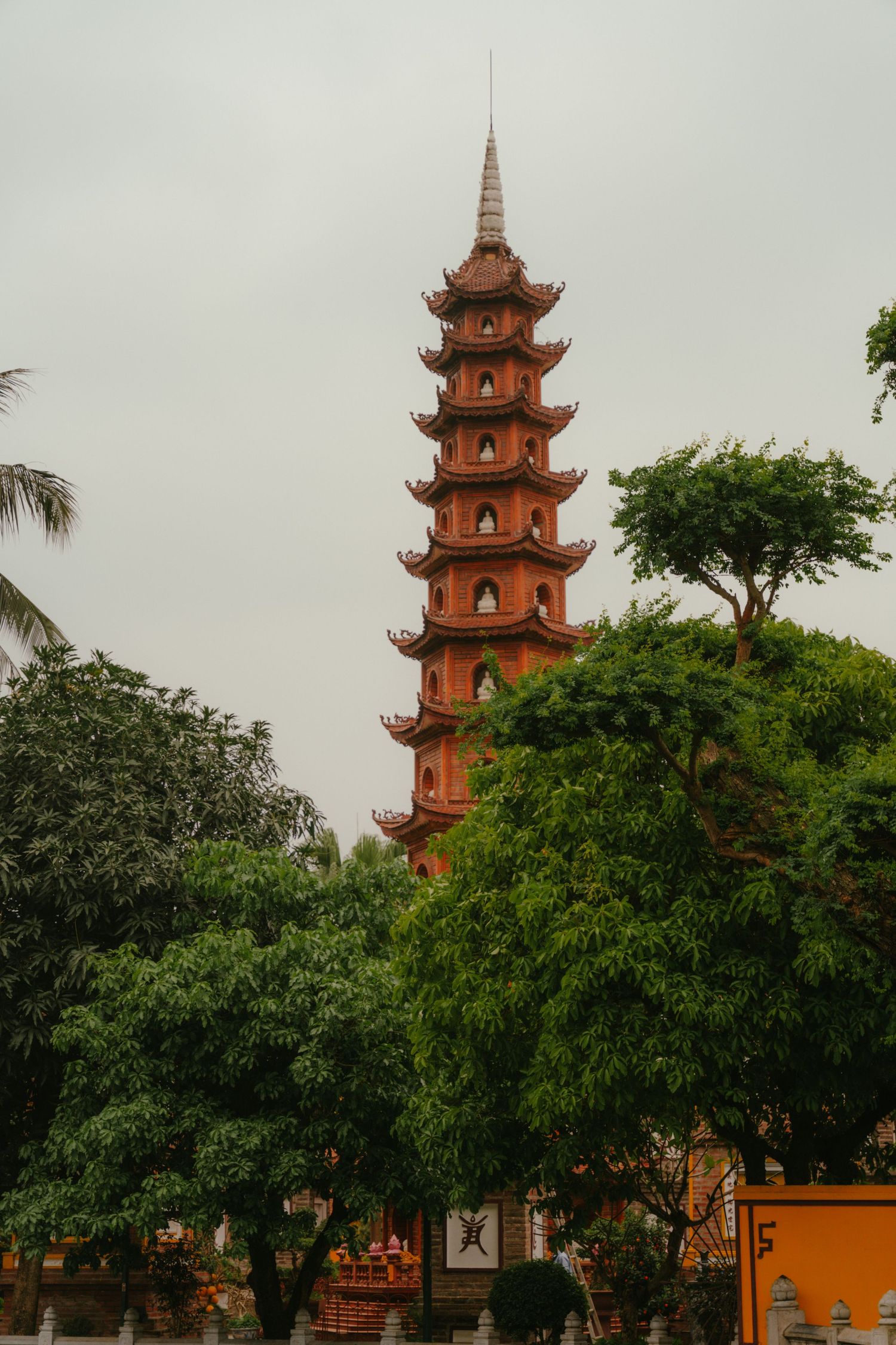 Tall orange pagoda tower rising above trees against an overcast sky in traditional Asian architectural style.