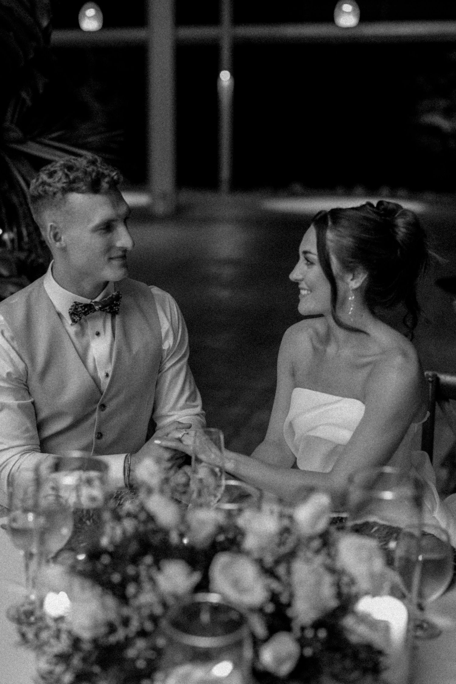 Black and white photo of couple having intimate conversation at decorated reception table.