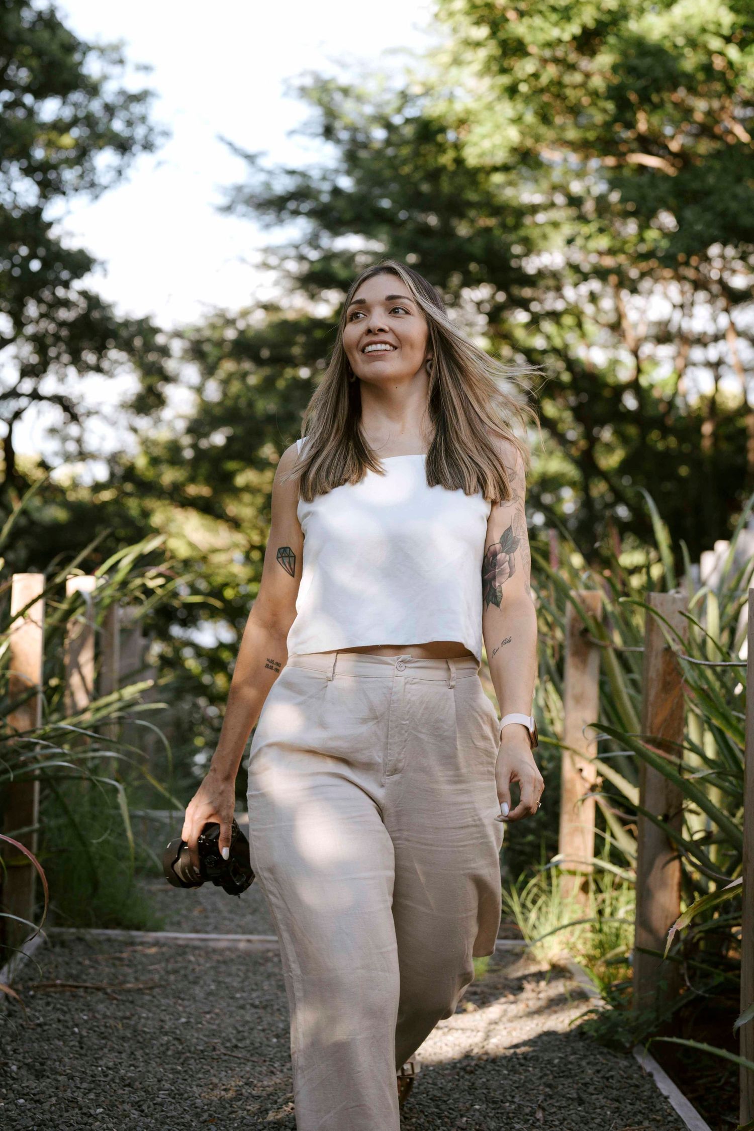 Person in casual beige outfit walking through a sunny garden path with trees.