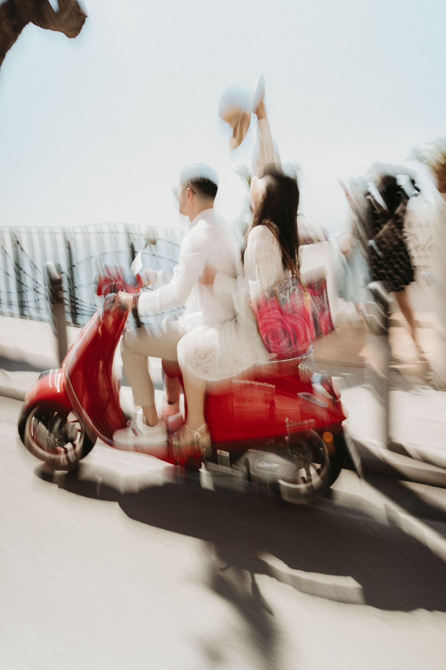Motion blur captures a red Vespa scooter and rider in a dynamic sequence of movement against a bright background.
