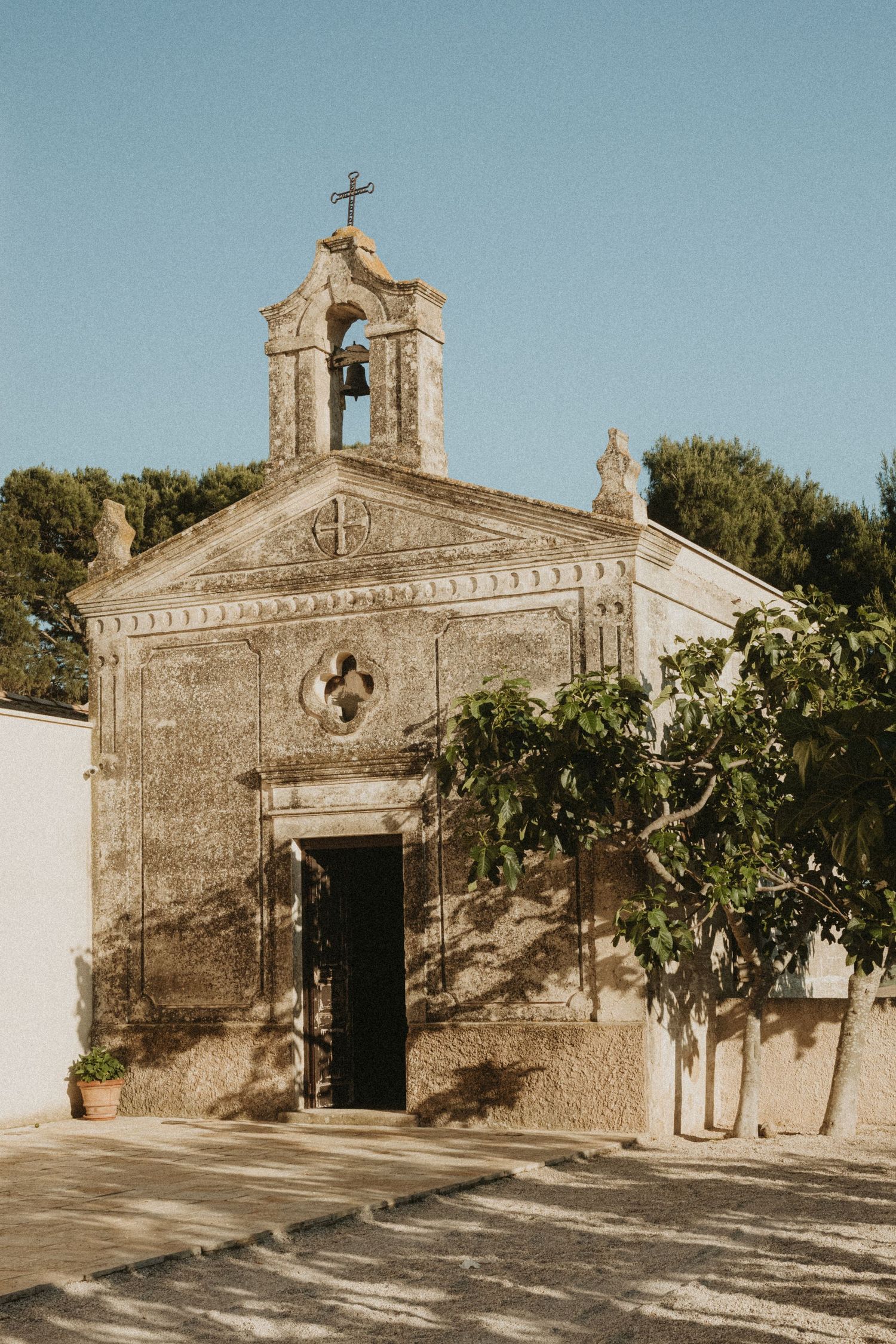 Four views of a rustic stone chapel with bell tower and cross in Mediterranean setting under sunlight.