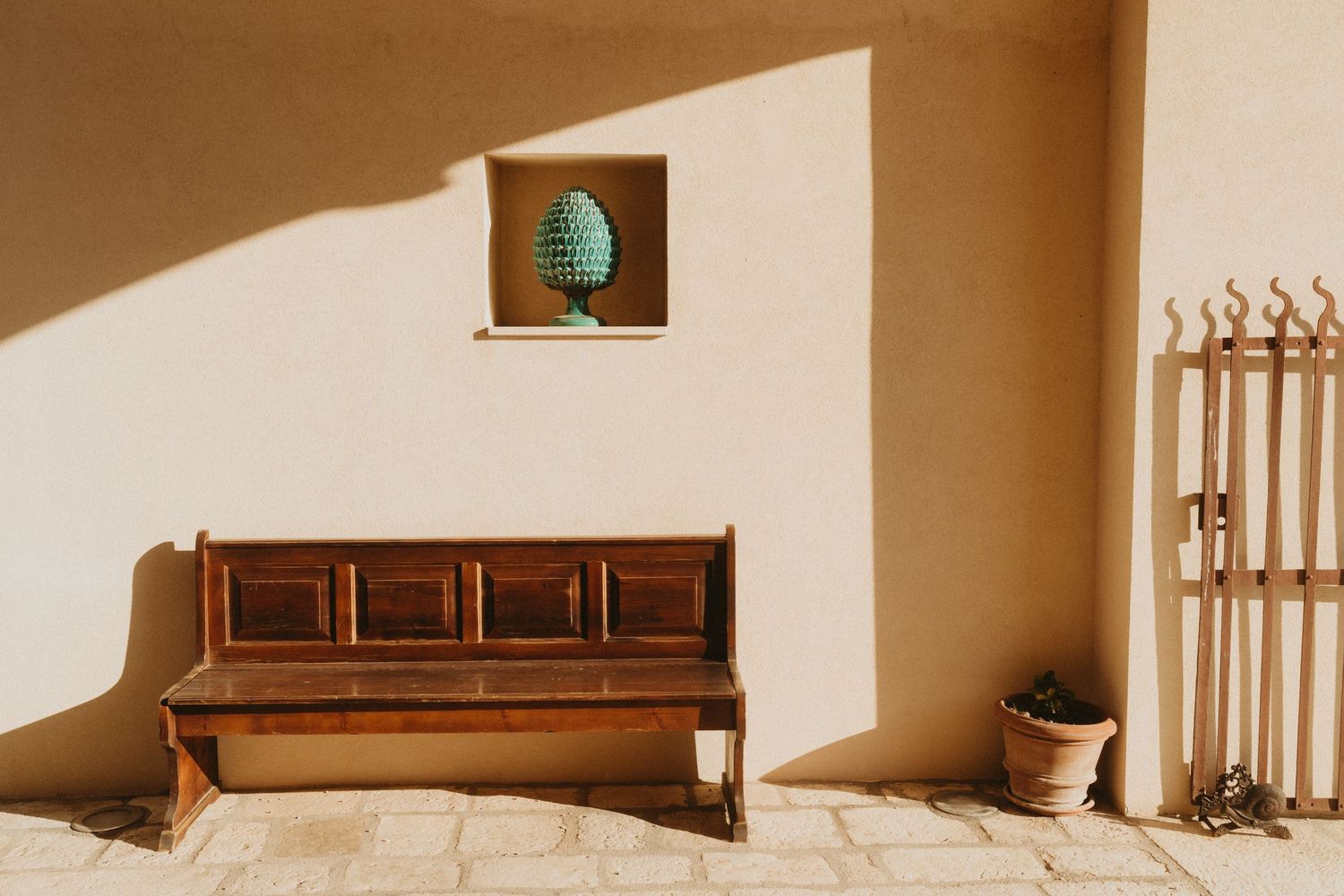 Wooden bench against beige wall with turquoise vase in recessed niche and decorative coat rack in corner.