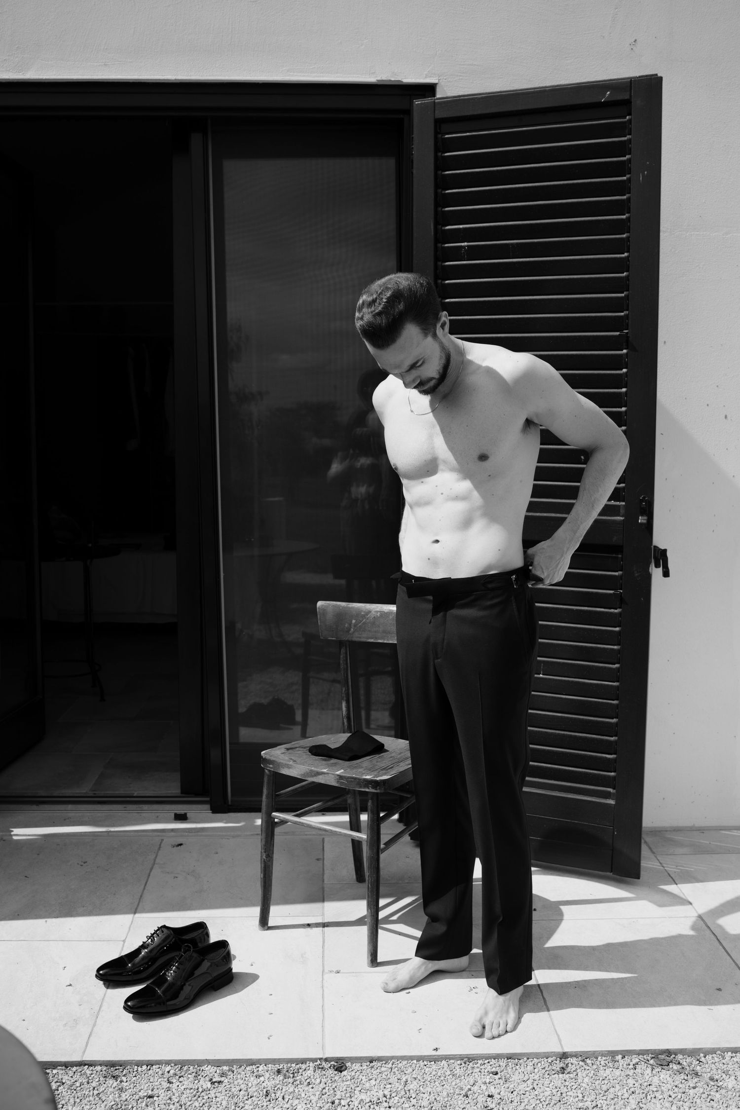 A black and white sequence showing someone putting on shoes while standing near a doorway with shutters.