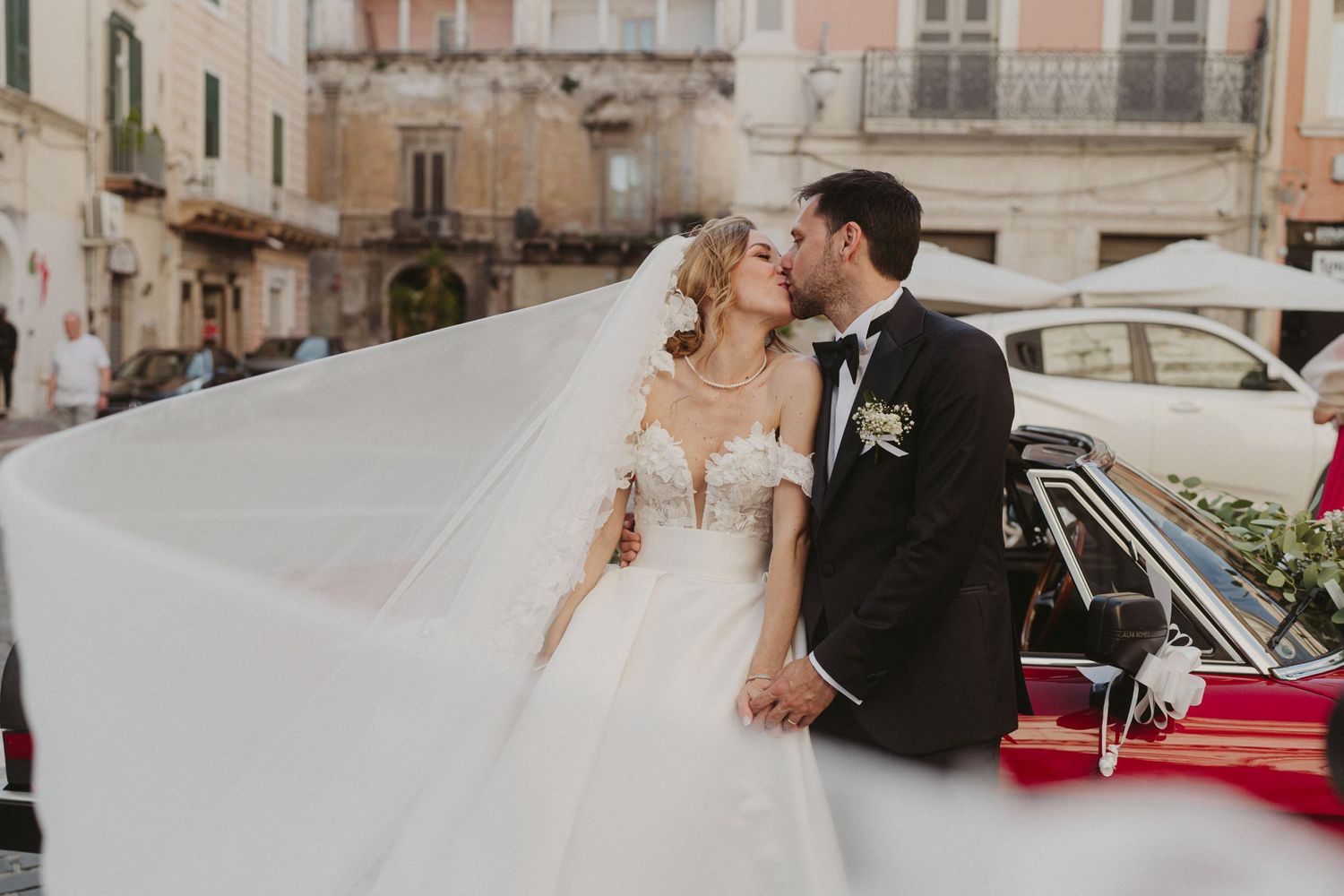 Wedding couple standing near vintage car on charming European cobblestone street.