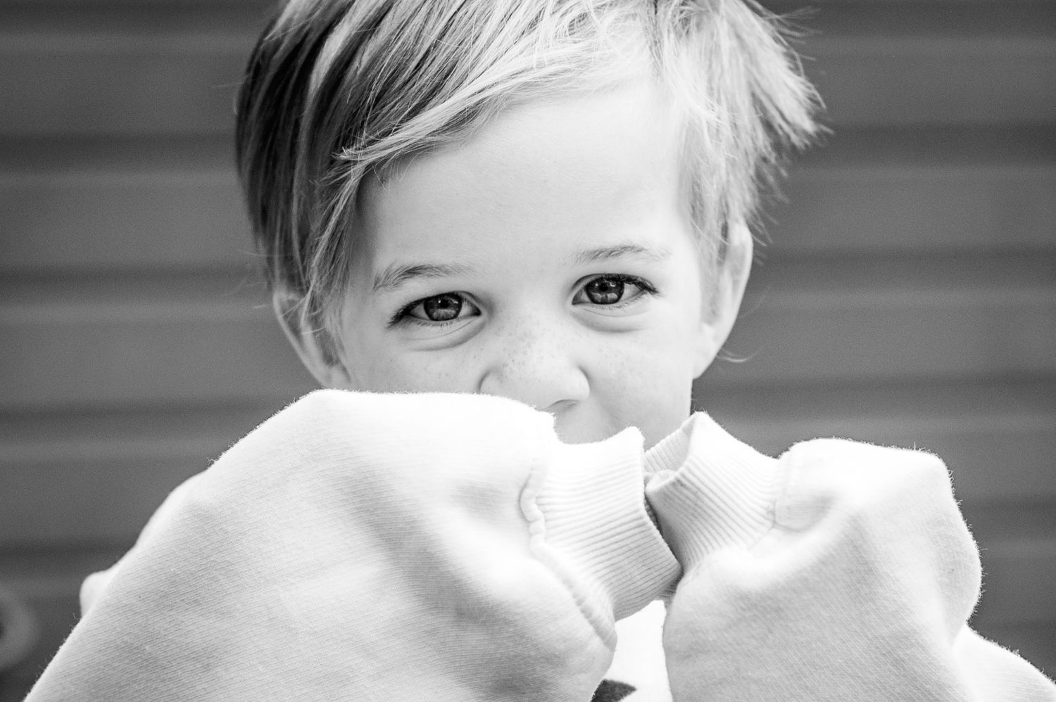 4 year old boy cheekily covering his mouth during a nursery photoshoot, in Ashtead, Surrey