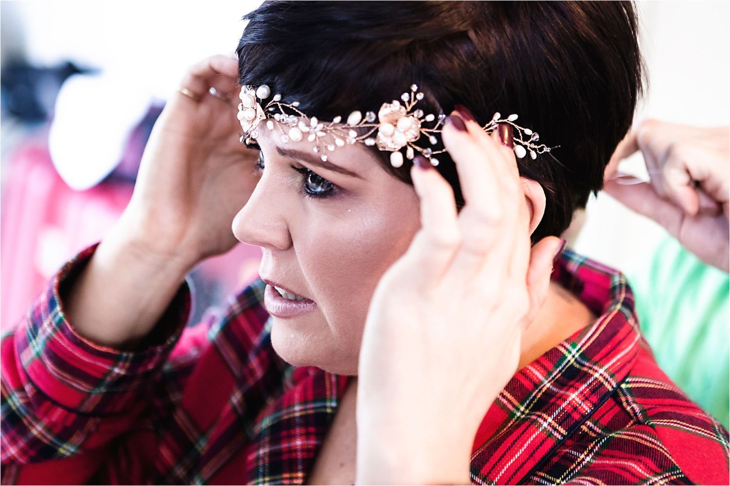 Someone in a red plaid shirt adjusts a delicate silver floral headpiece while getting ready.