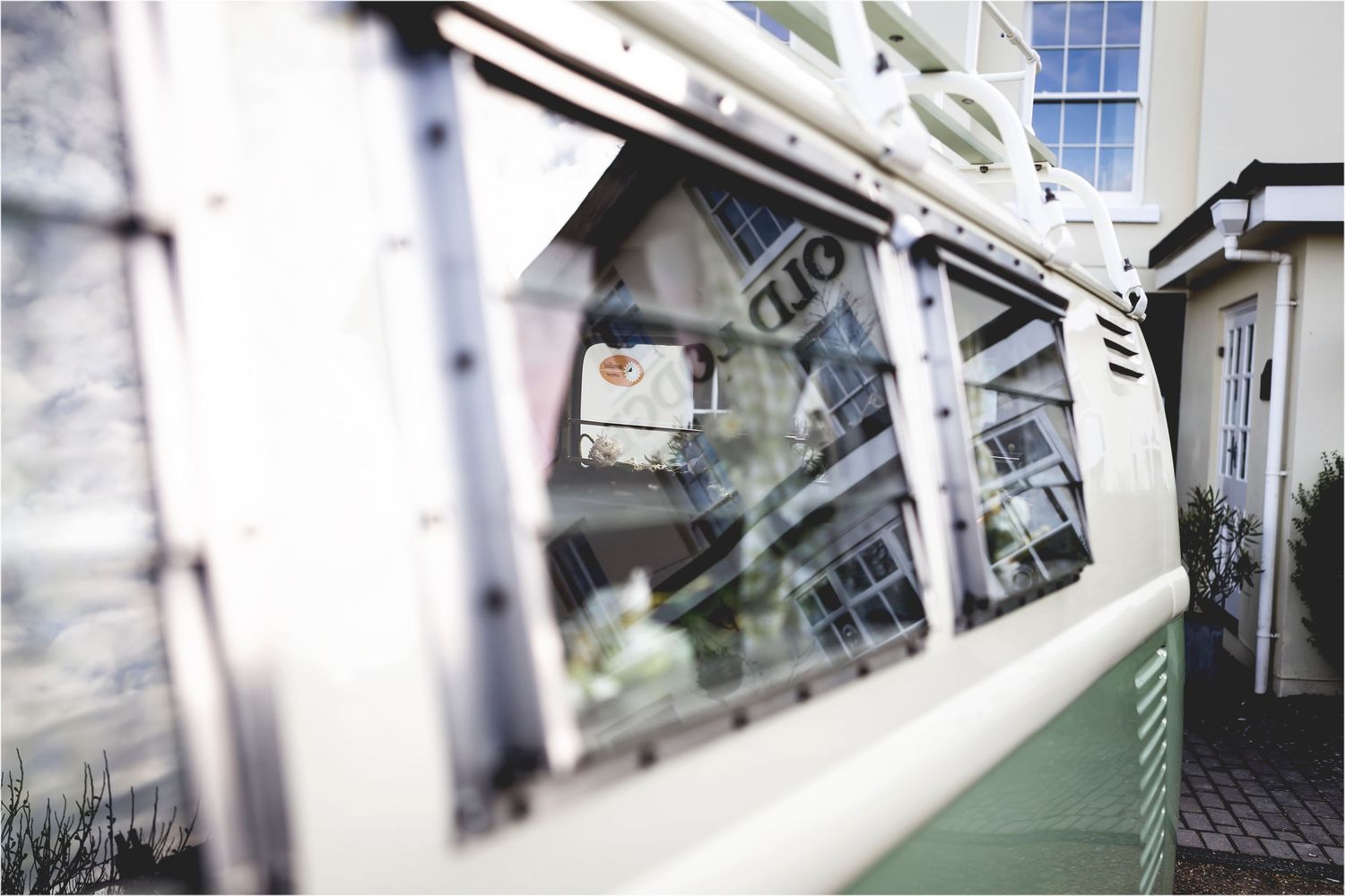 Close-up view of a vintage green and white VW van window showing reflective glass and metallic frame details.