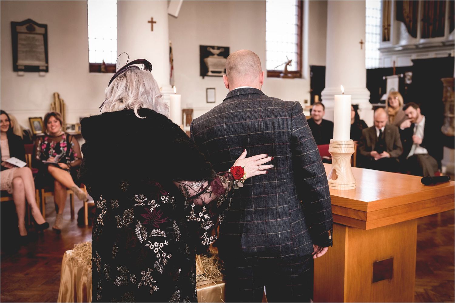 Two people stand arm in arm during a church ceremony while others sit in pews watching.