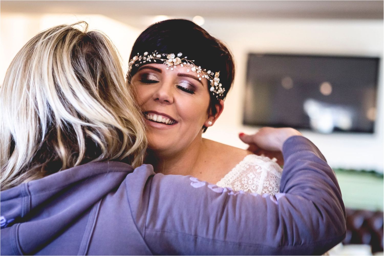 A touching embrace between friends during a celebration, with one wearing a delicate bridal headpiece with crystals.