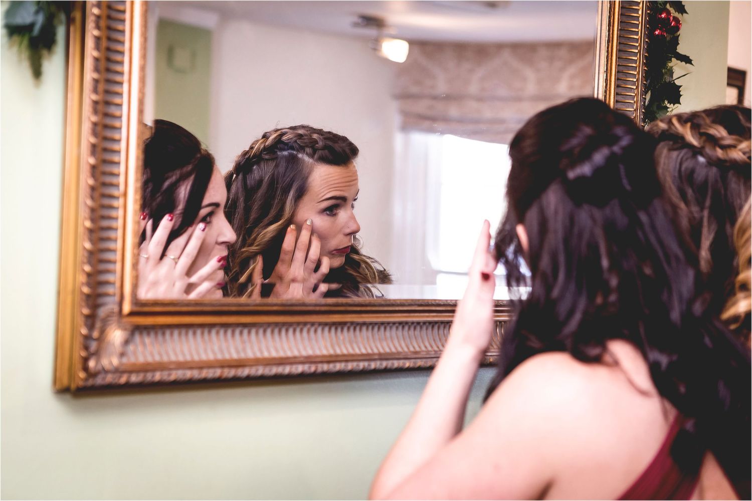Dark-haired individual getting ready in front of an ornate gold-framed mirror while styling hair.