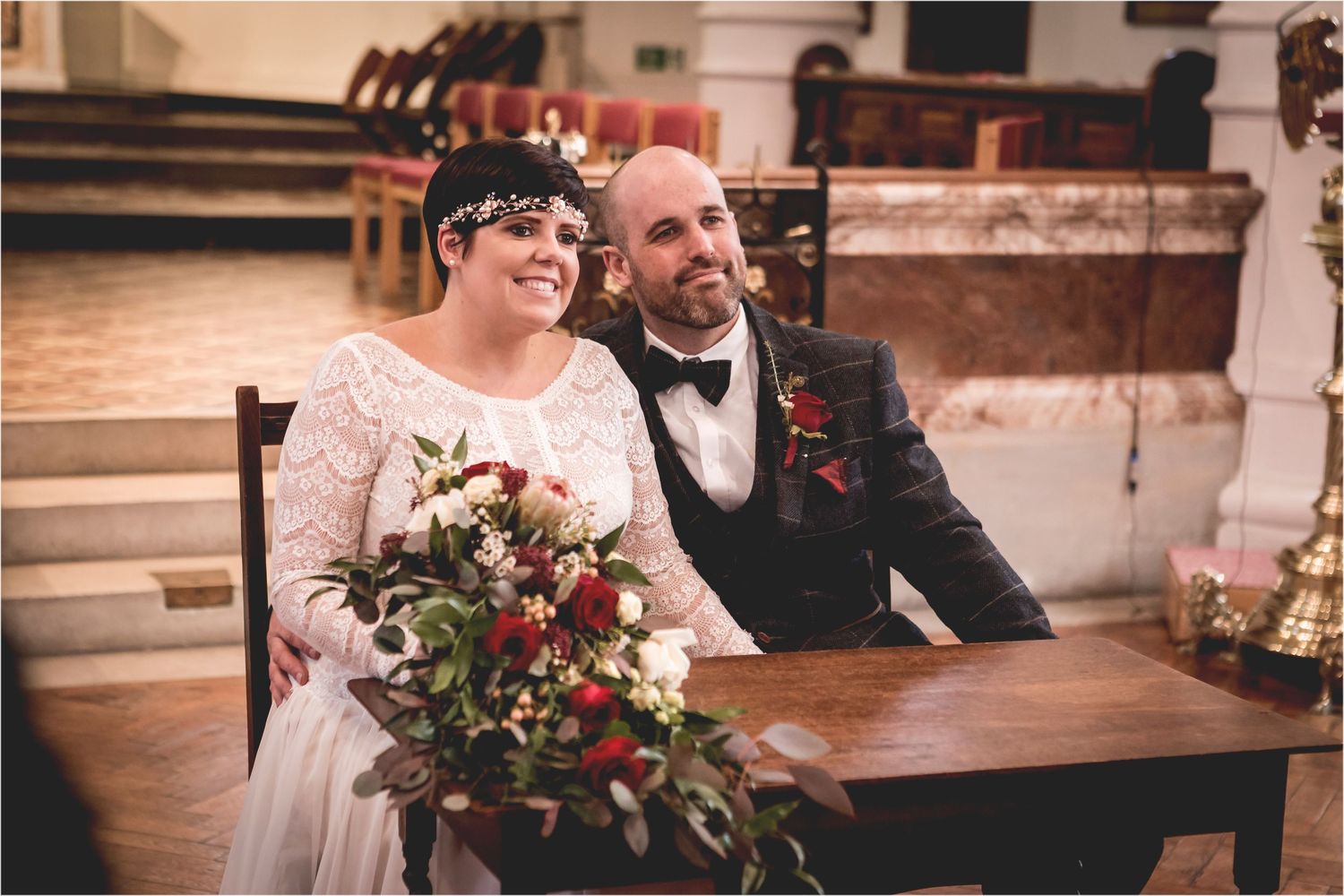 A couple sitting together at a wooden table during their wedding celebration in a church setting.