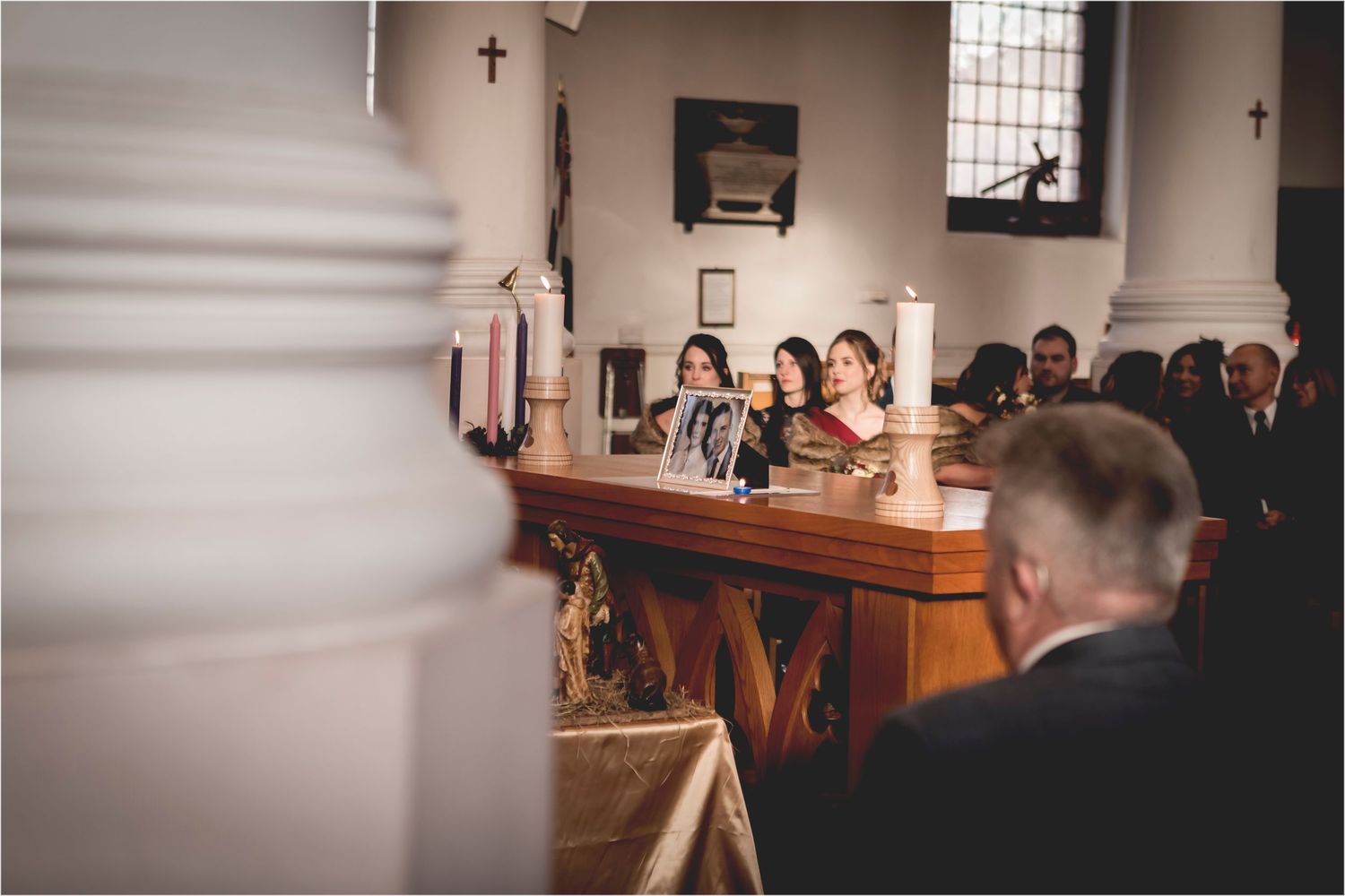 A church interior during a religious ceremony with worshippers seated in wooden pews and candles glowing on the altar.