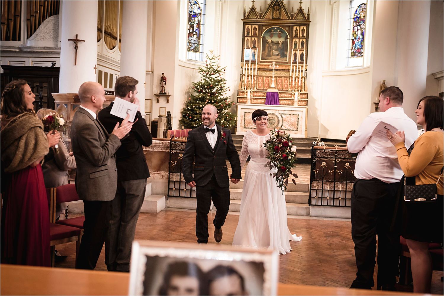A wedding ceremony in a traditional church with guests watching and a decorated Christmas tree in the background.