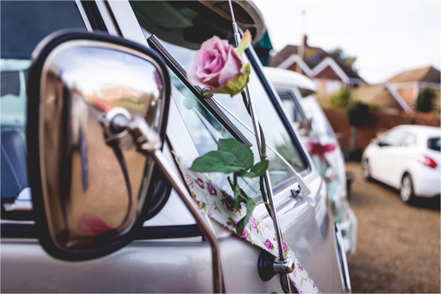 Pink rose flower attached to car mirror for wedding decoration, with vehicles parked in background.
