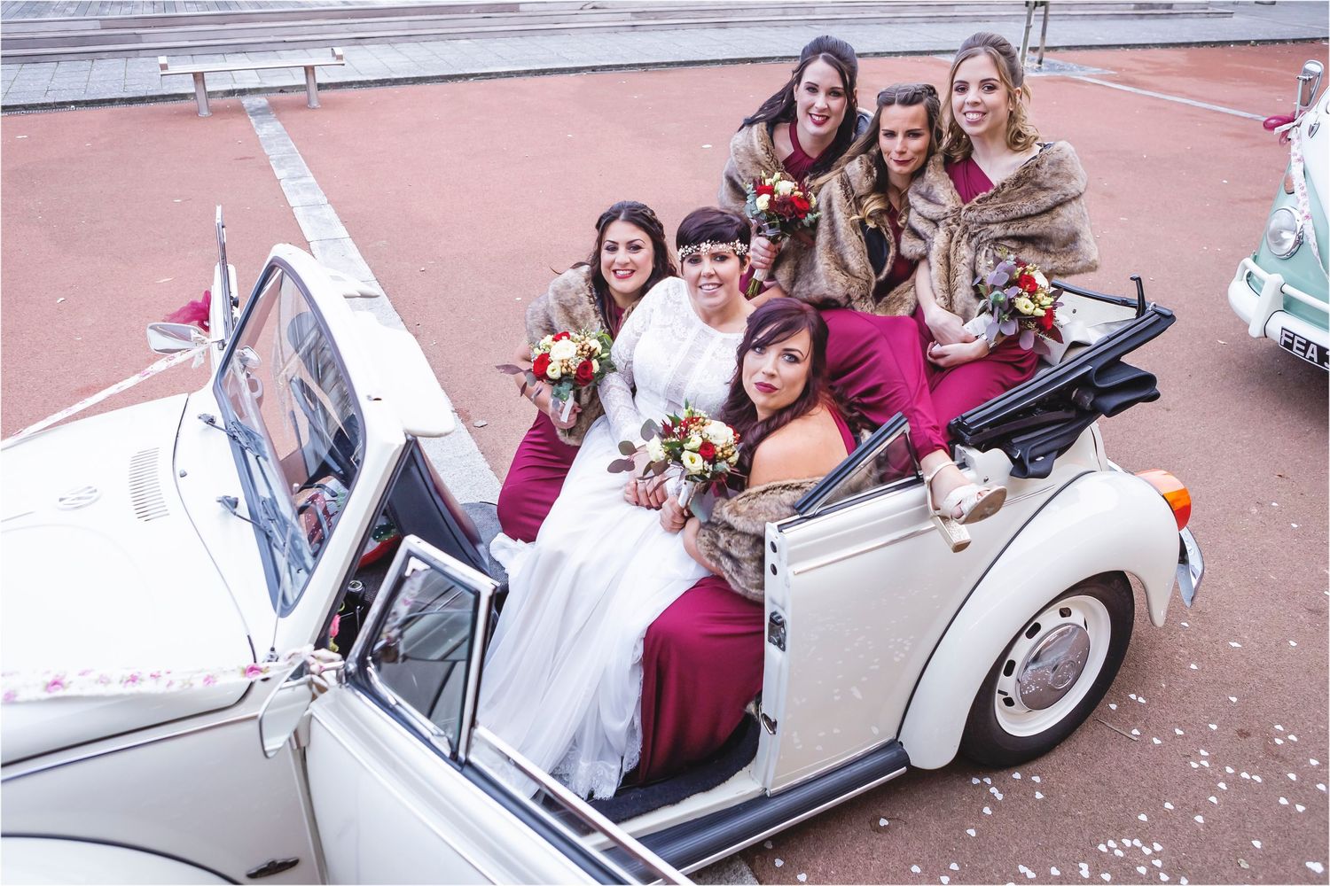 A classic white vintage convertible car decorated for a wedding celebration on a pink-toned street.