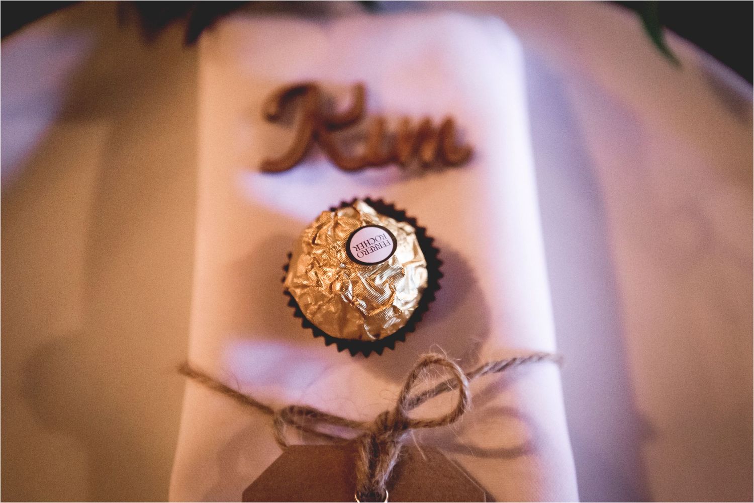 A single Ferrero Rocher chocolate wrapped in gold foil with a rustic twine bow on a white surface.
