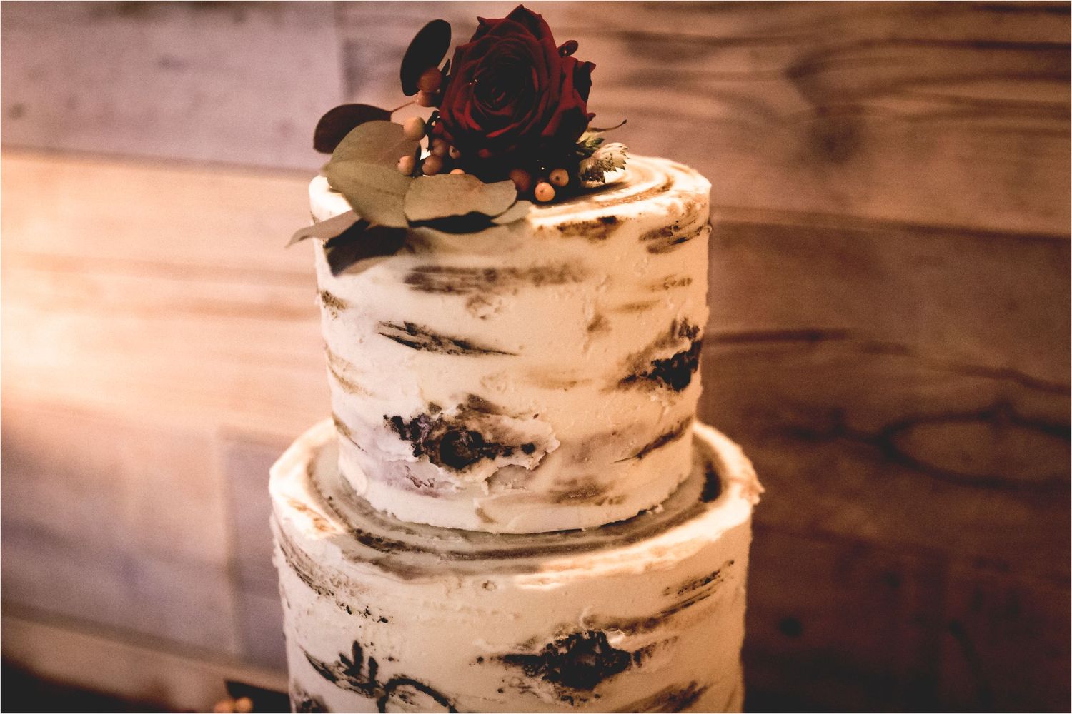 A rustic-style wedding cake with semi-naked buttercream frosting and dark berries displayed on a wooden table.