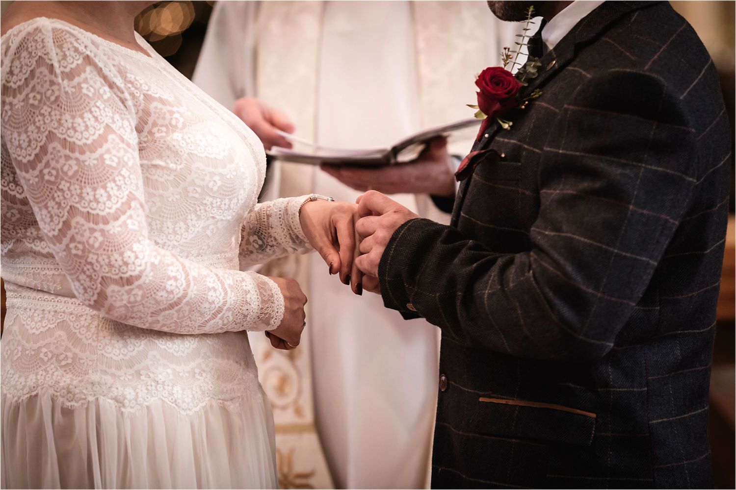 Close-up of a couple holding hands at a wedding ceremony with a white lace dress and black suit.
