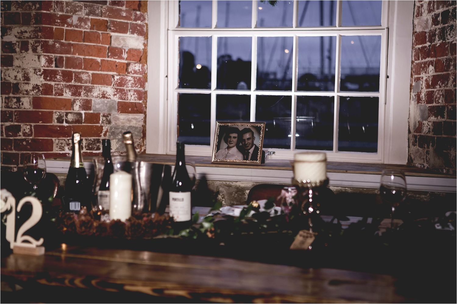 A rustic window display with wine bottles and decorative elements on a wooden surface against exposed brick walls.