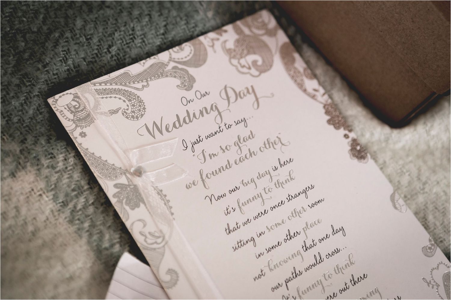 An elegant wedding program with delicate swirling paisley designs printed in gray on light pink paper.