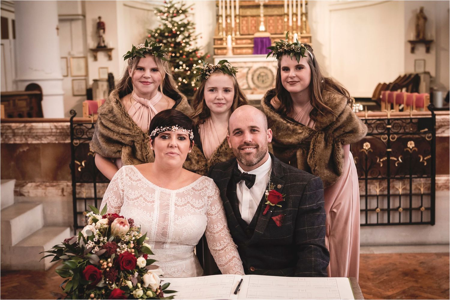 A festive wedding ceremony in a church with a decorated Christmas tree and holiday decor in the background.