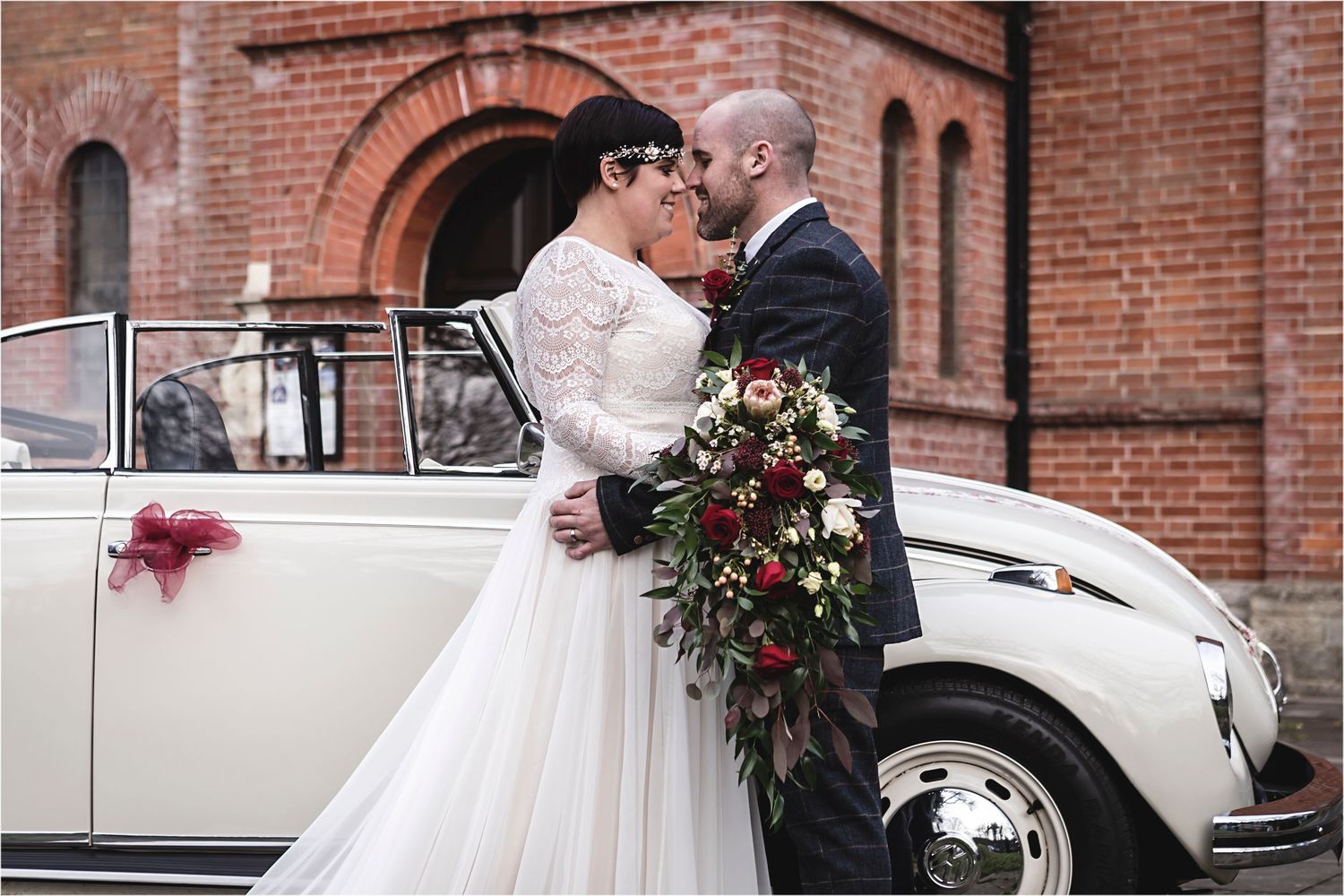 A classic white vintage car adorns a romantic winter wedding scene against a brick building backdrop.