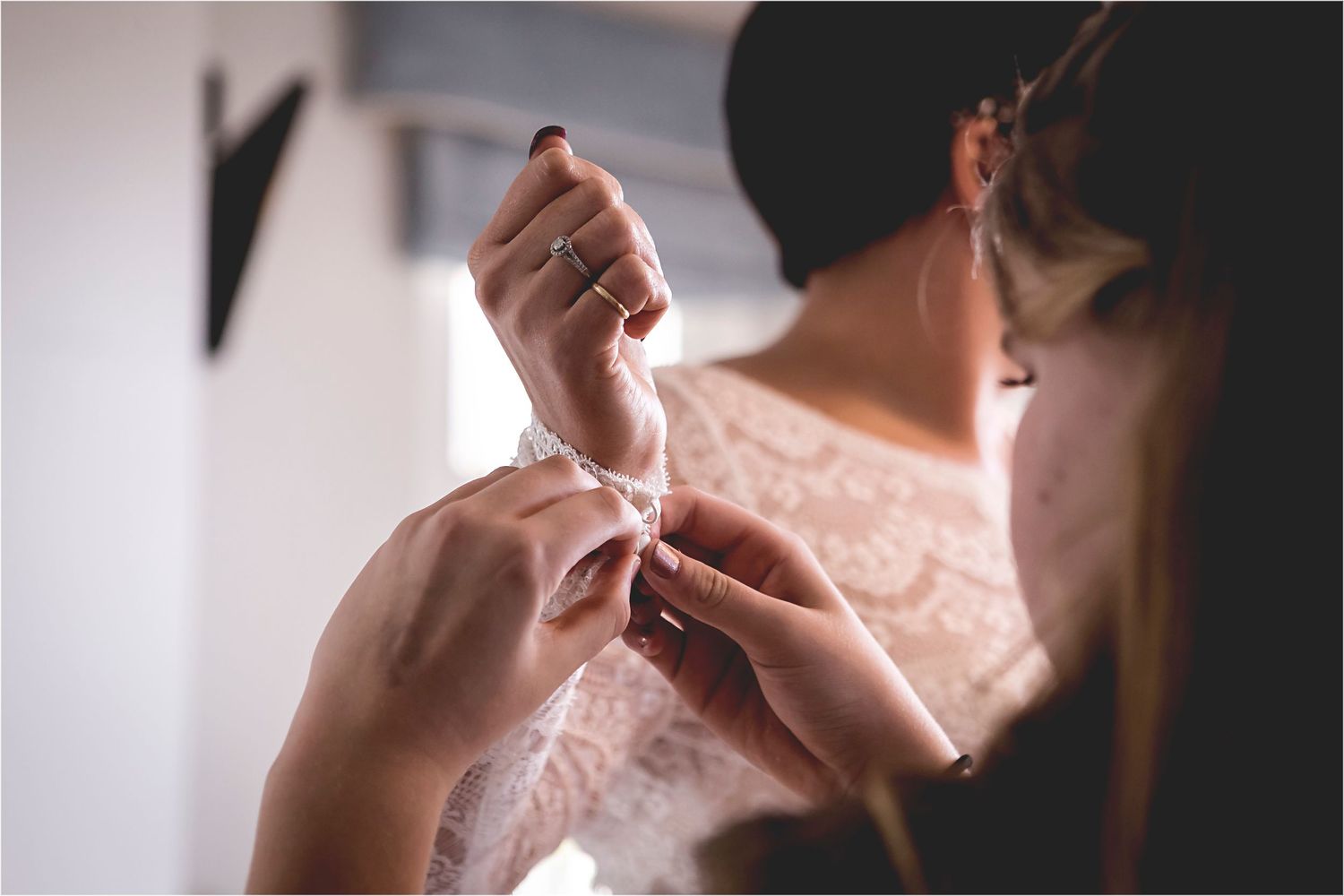 Close up of hands fastening delicate buttons on a light pink lace garment in soft natural lighting.