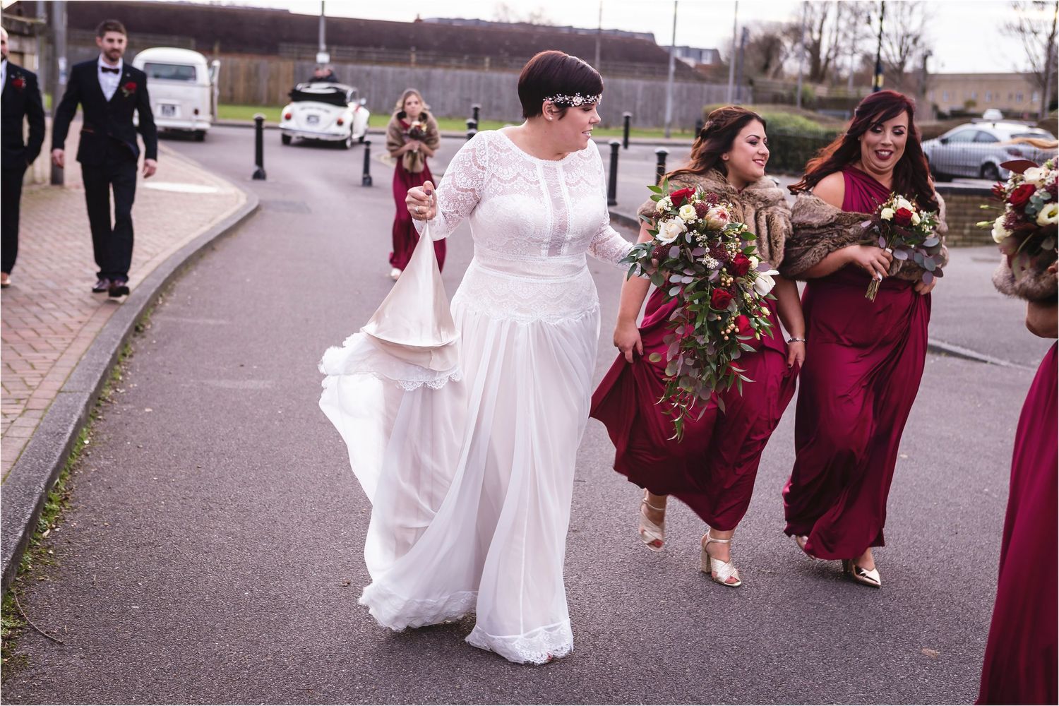 Wedding party walking down street with bridesmaids in burgundy dresses holding bouquets.