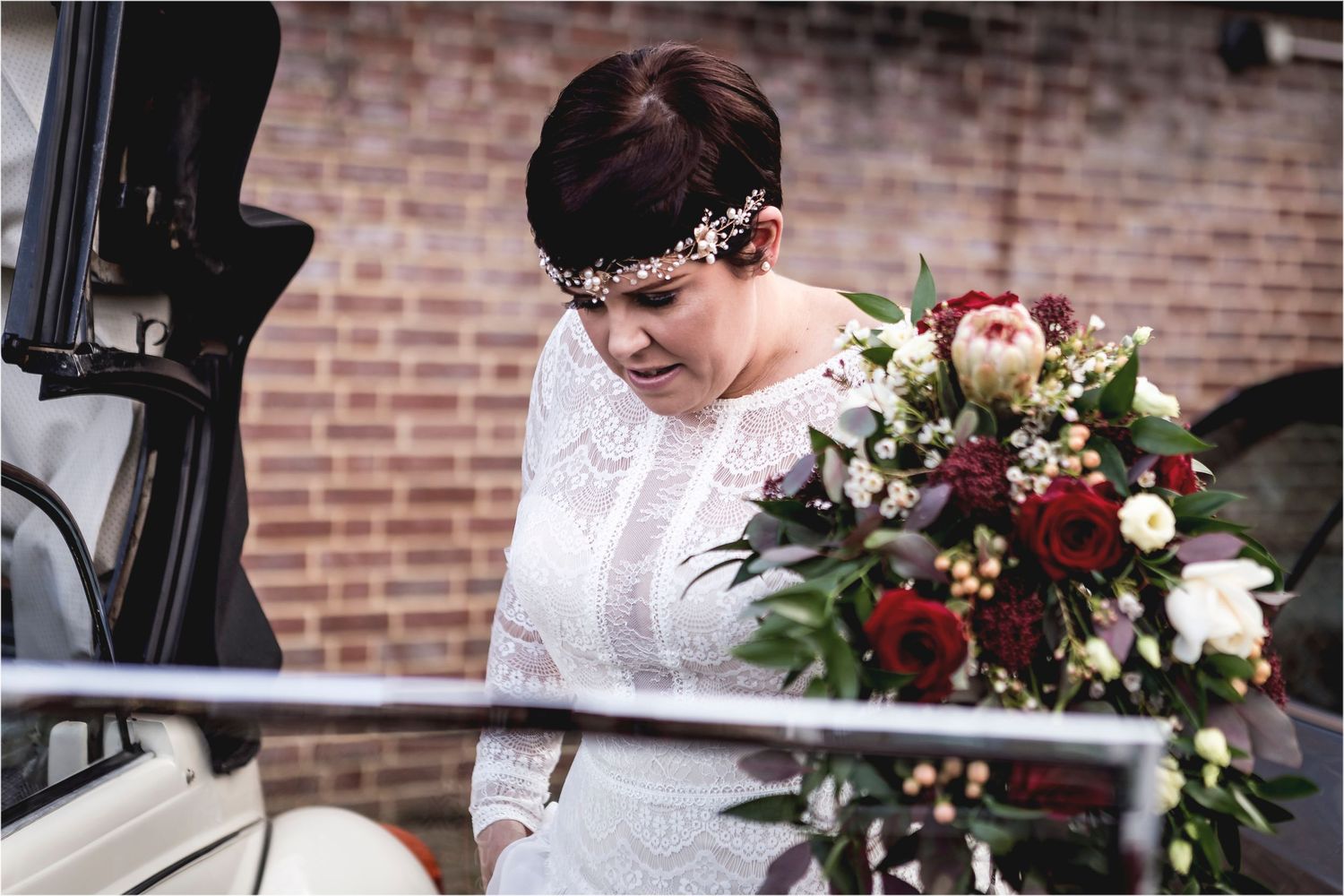 A person in white lace dress and crystal headpiece holding a rich burgundy and blush floral wedding bouquet.