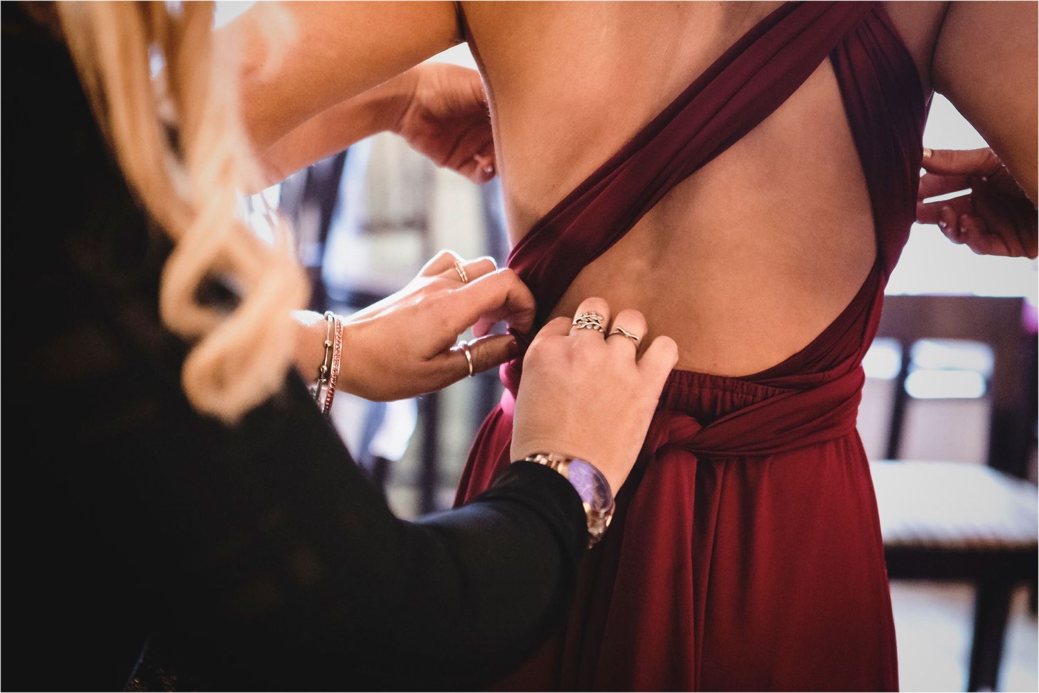 Hands adjusting the back of a burgundy formal dress during a fitting session.