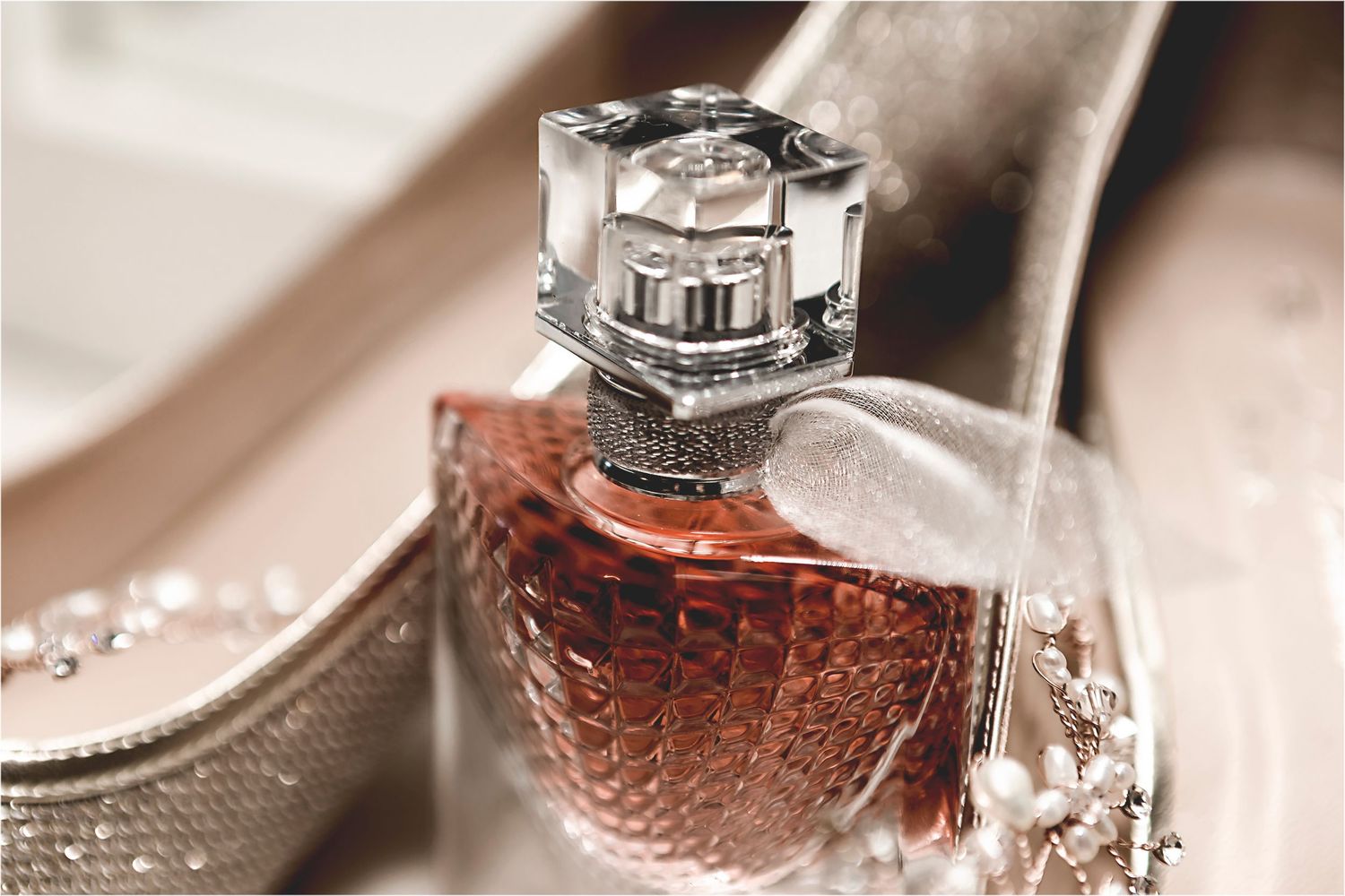 Elegant crystal perfume bottle with ornate metallic cap and rose-colored fragrance in vintage styling photography.