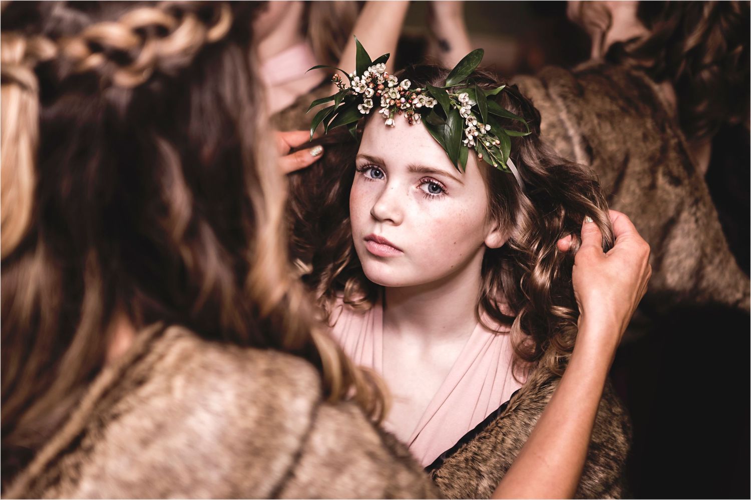 Ethereal portrait of someone wearing a delicate leaf crown and pink dress against a moody brown backdrop.