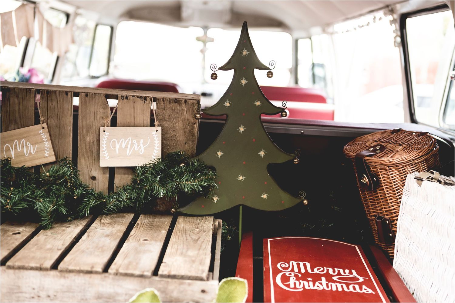 Rustic Christmas decorations including wooden tree and signs arranged in back of vintage vehicle with festive greenery.