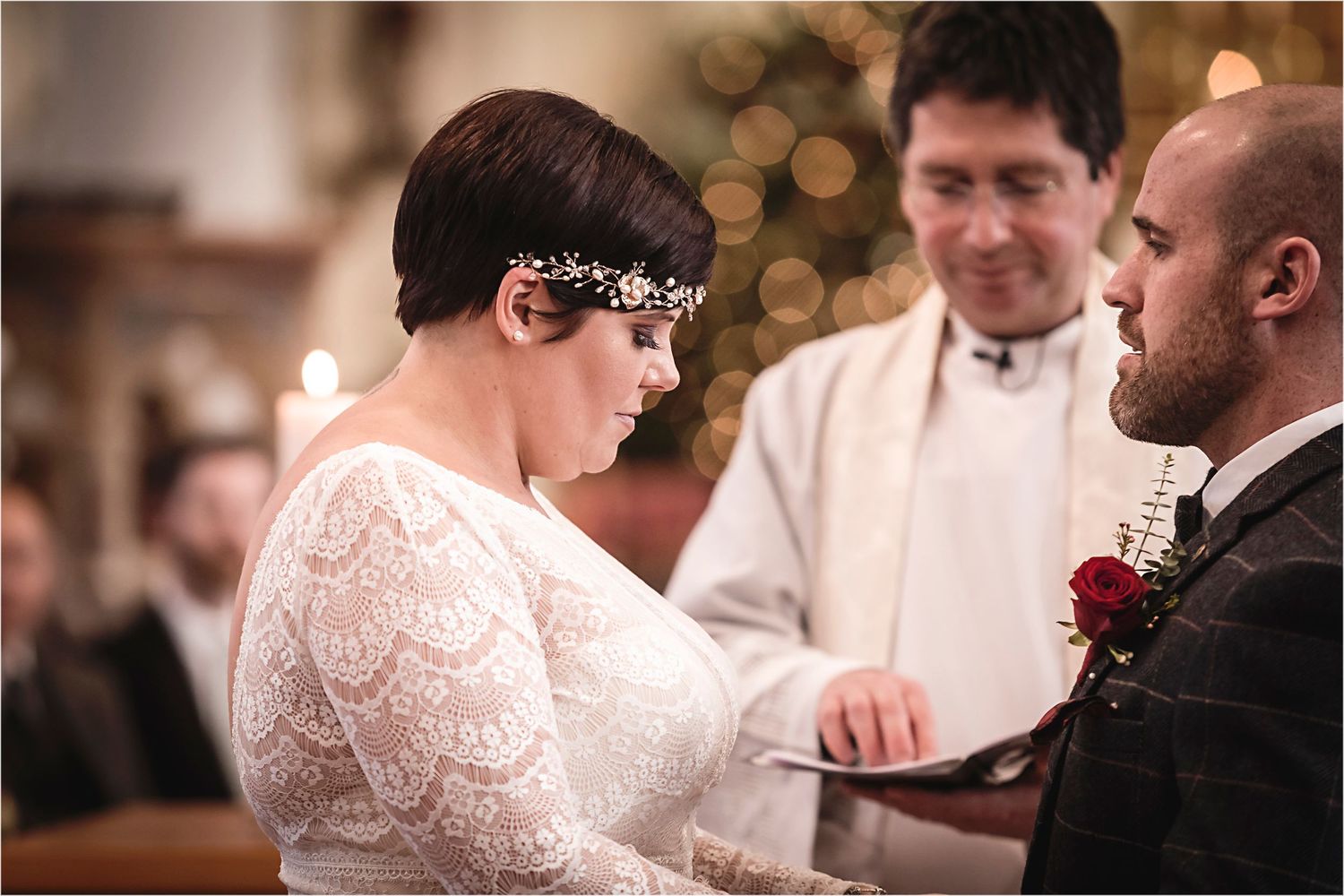 A couple exchanges vows during an intimate wedding ceremony with an officiant in a candlelit setting.