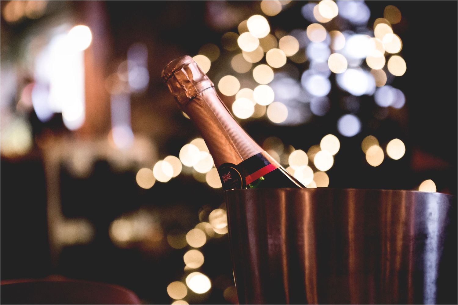 Champagne bottle in an ice bucket with festive bokeh lights creating a romantic holiday atmosphere in background.