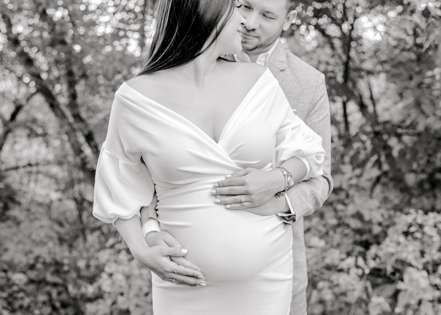 husband standing behind his wife as they look at each other smiling, both cradling her baby bump