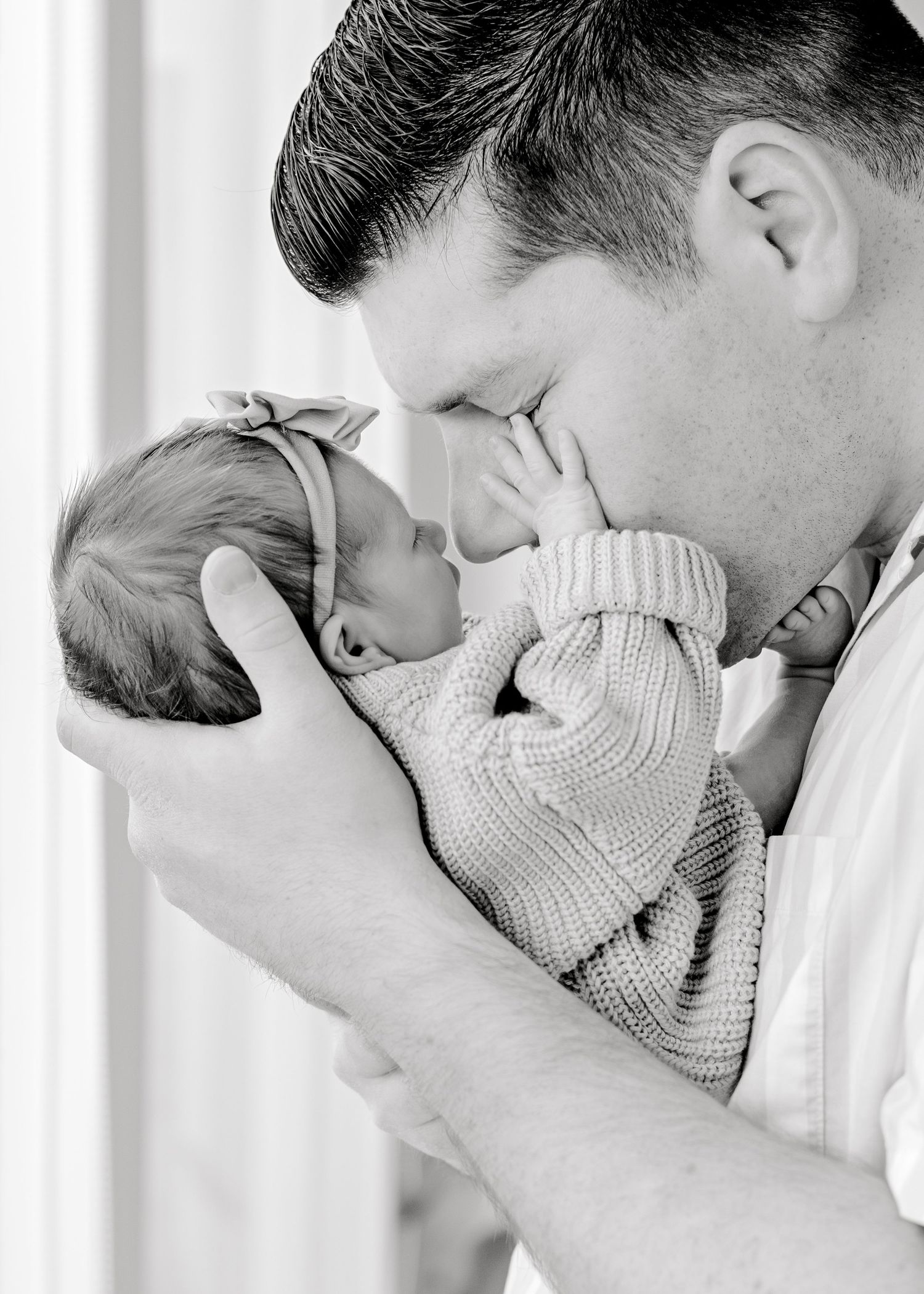dad going nose to nose with his newborn girl, as her little hand rests on his cheek