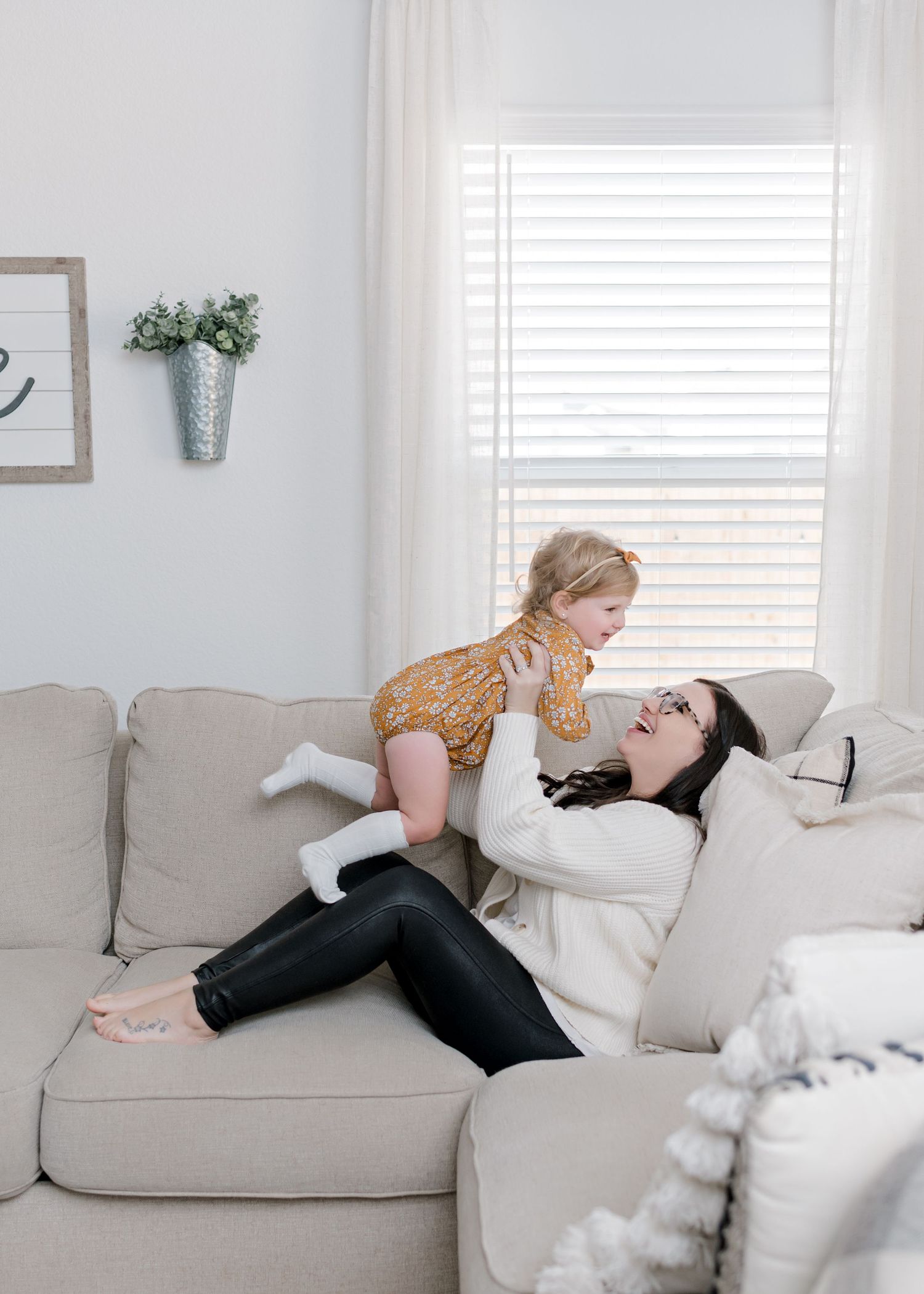 mom sitting on couch as she lifts her young daughter in the air