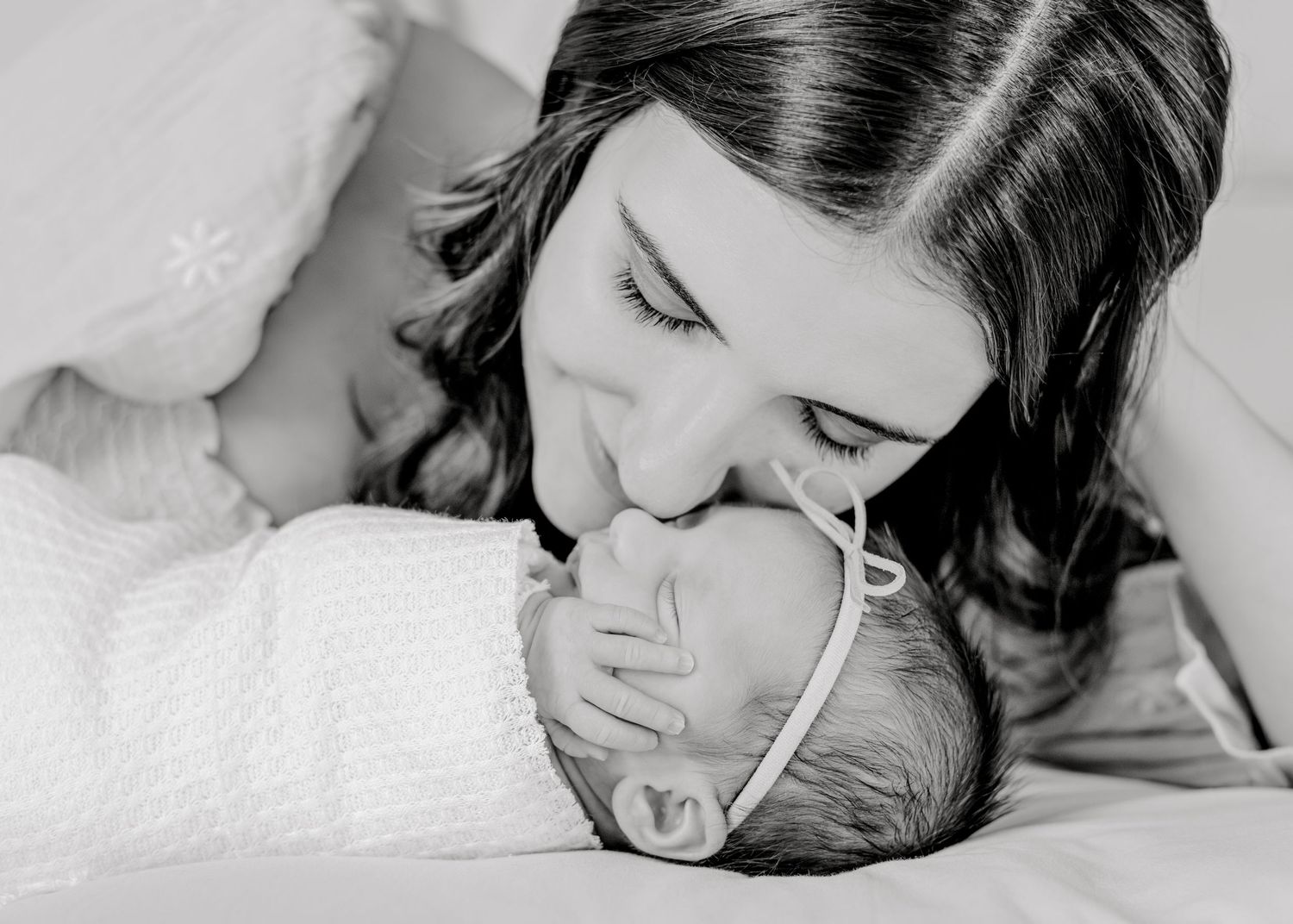 mom resting nose on her newborn baby's nose as baby girl's hand rests on her own cheek