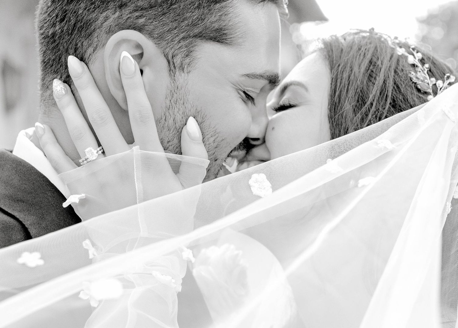 A romantic black and white photo of a couple kissing behind a sheer white veil.