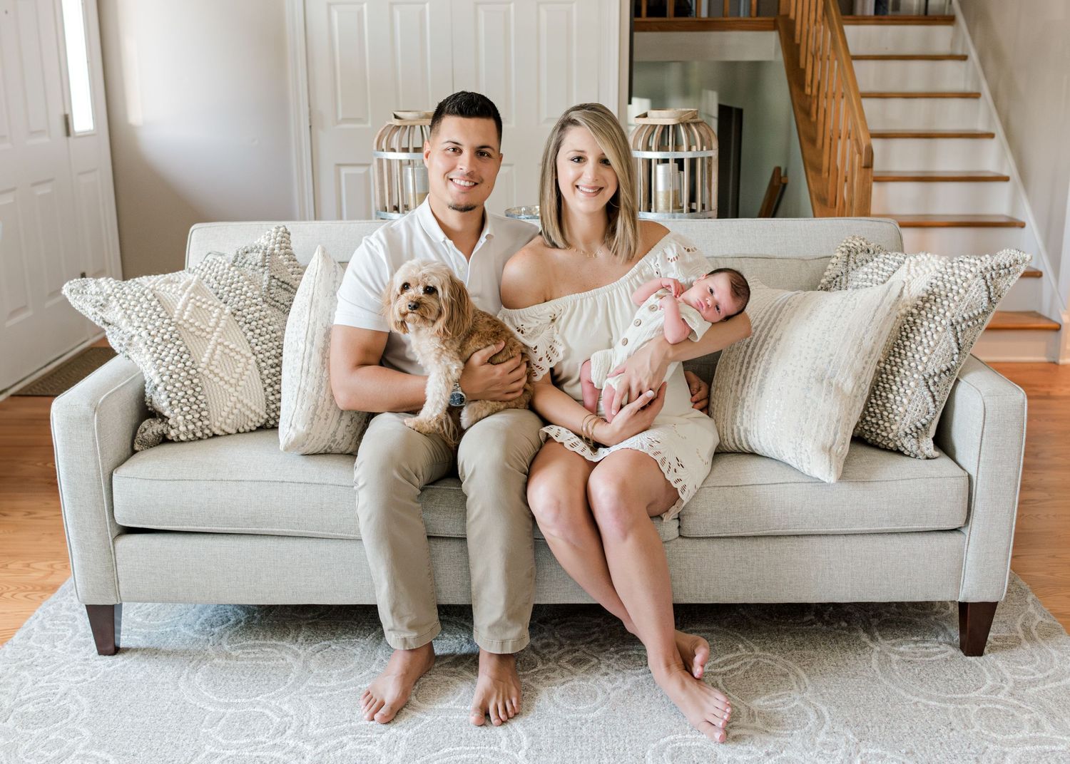 parents sitting on their couch with their new baby boy and their dog while smiling at the camera