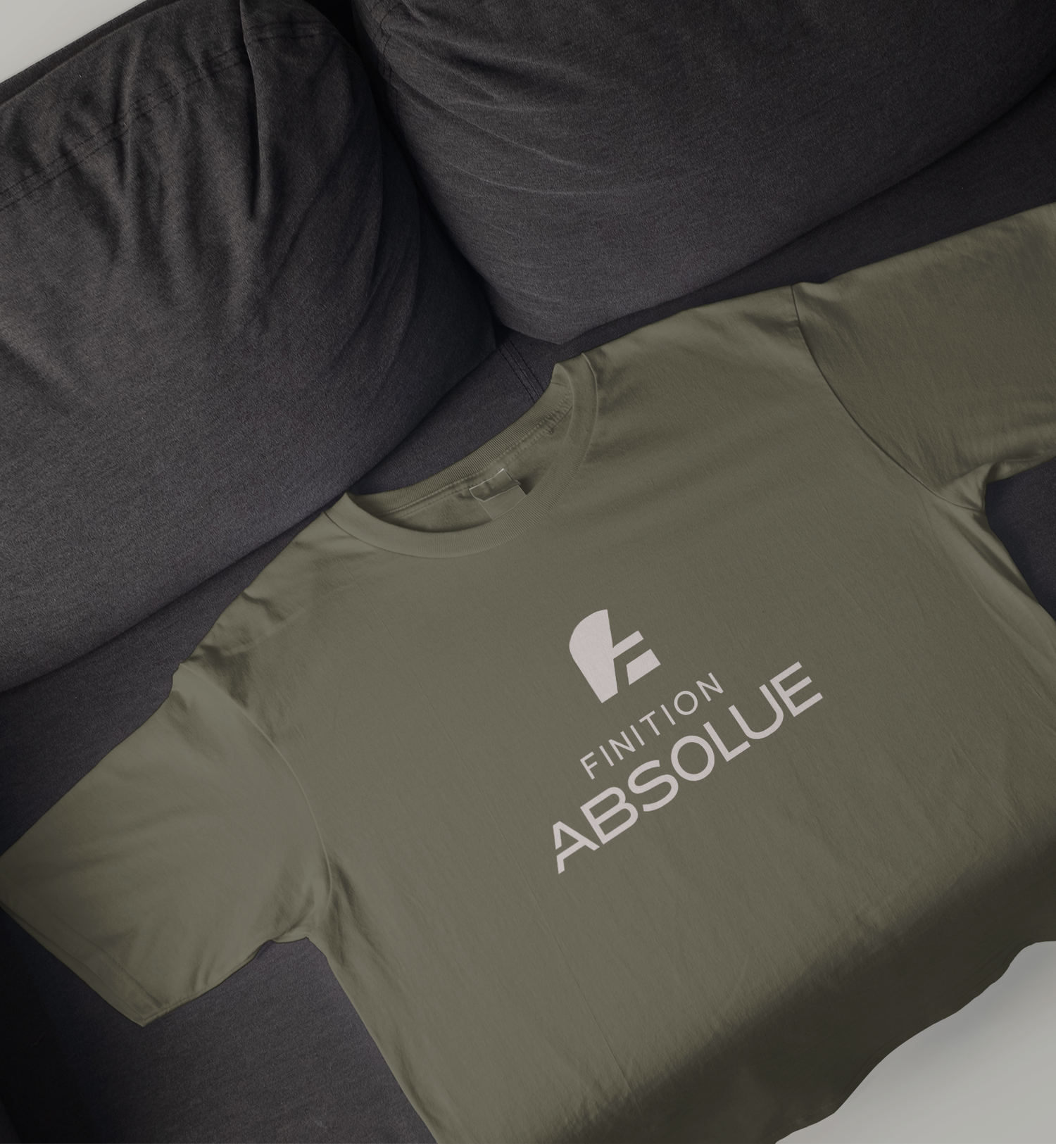 Olive green Finition Absolue logo t-shirt laid flat on a dark gray couch.