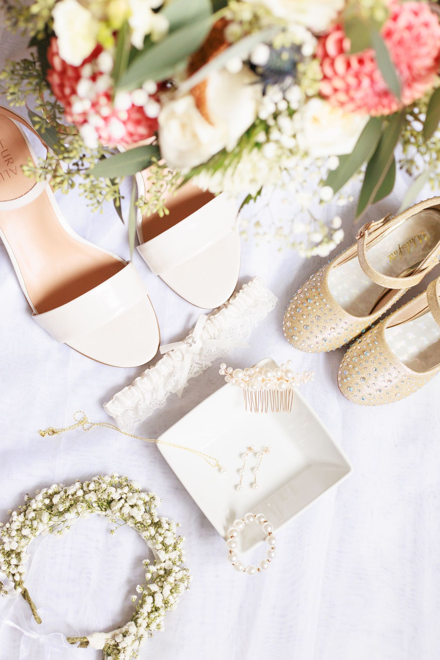 elegant wedding flatlay featuring bridal shoes, daughter's shoes, bouquet, and headpiece