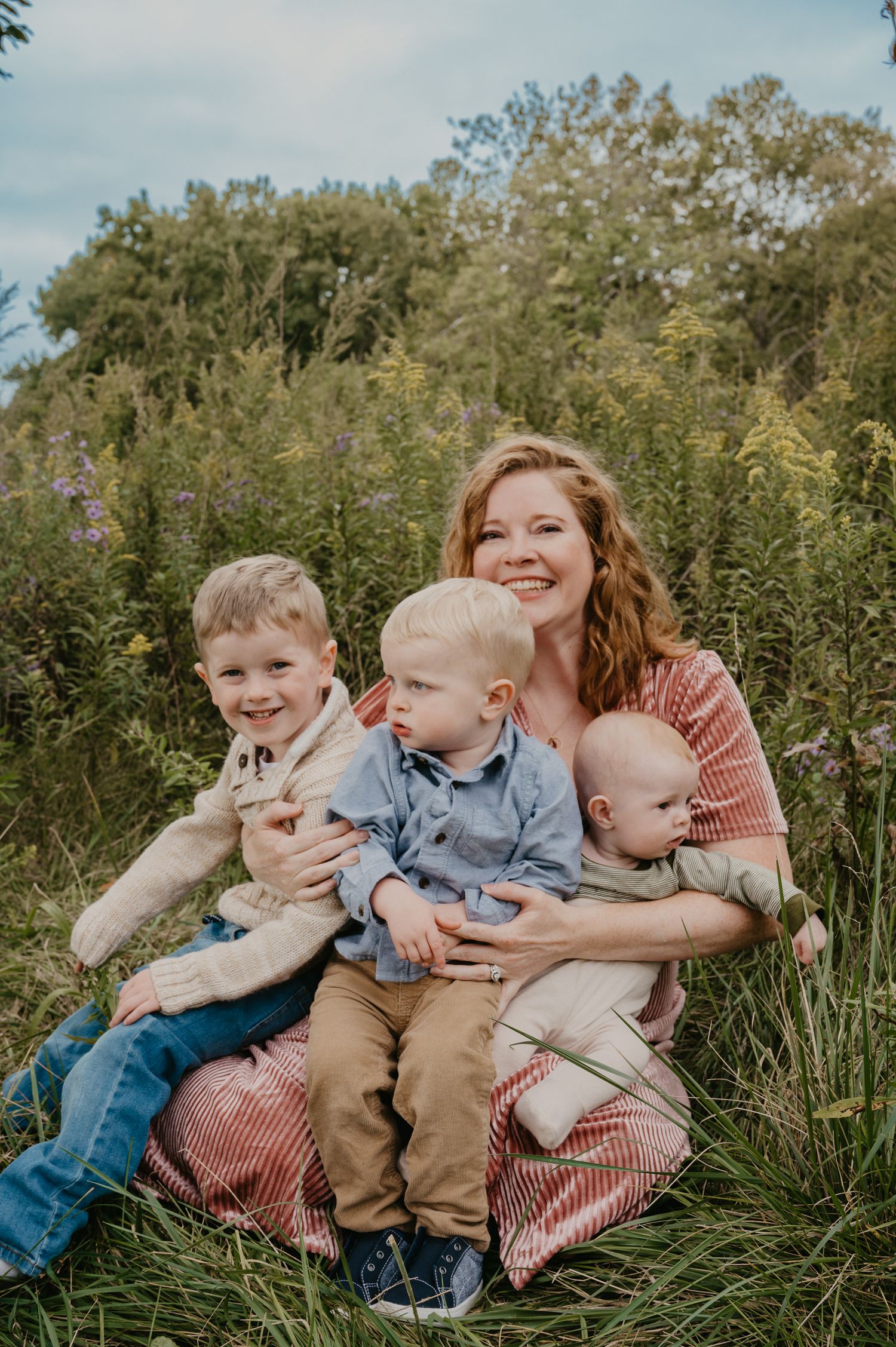 Smiling mother sitting in a meadow with her three young sons on a sunny day.