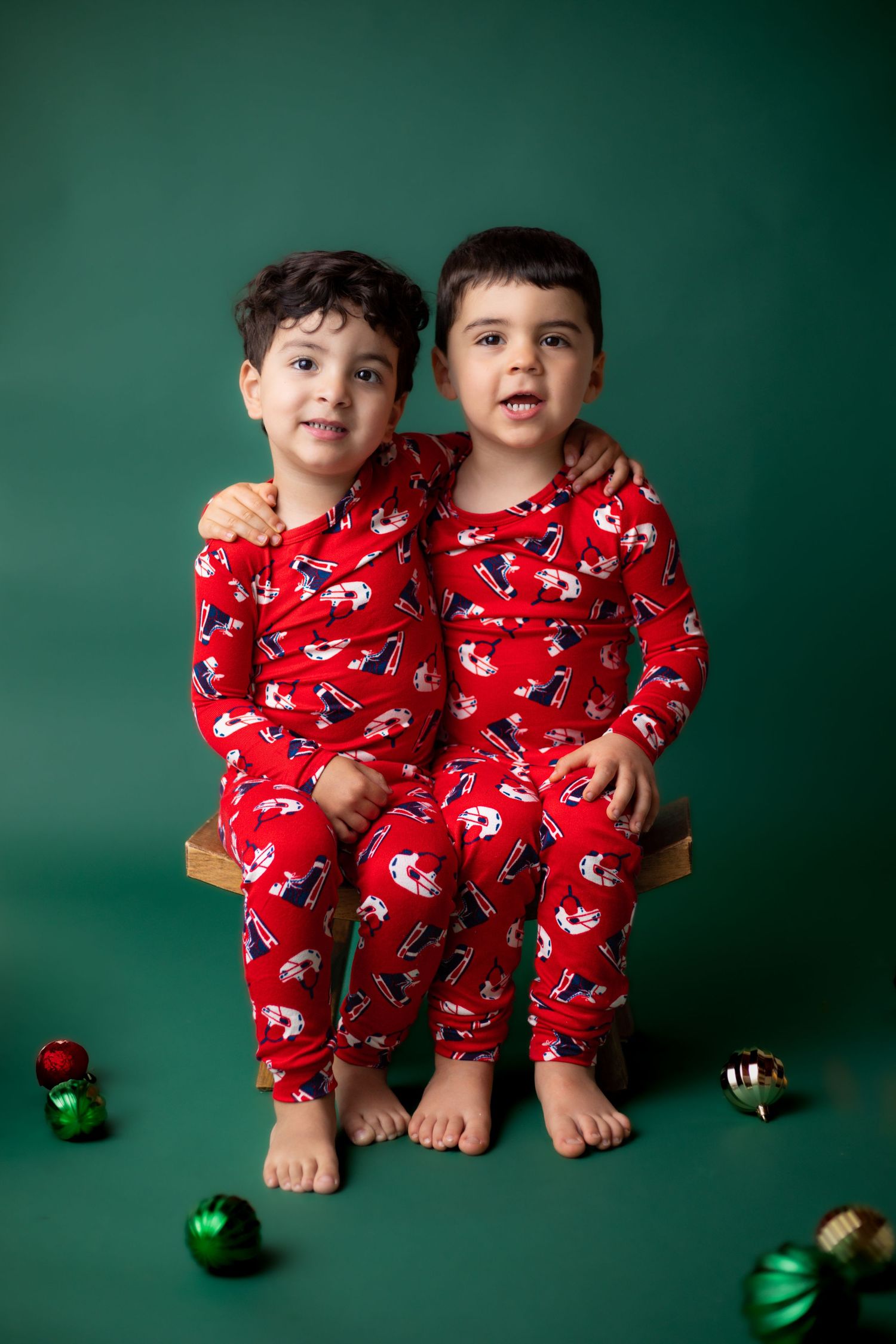 Young children in matching red holiday pajamas sitting on bench with Christmas ornaments.