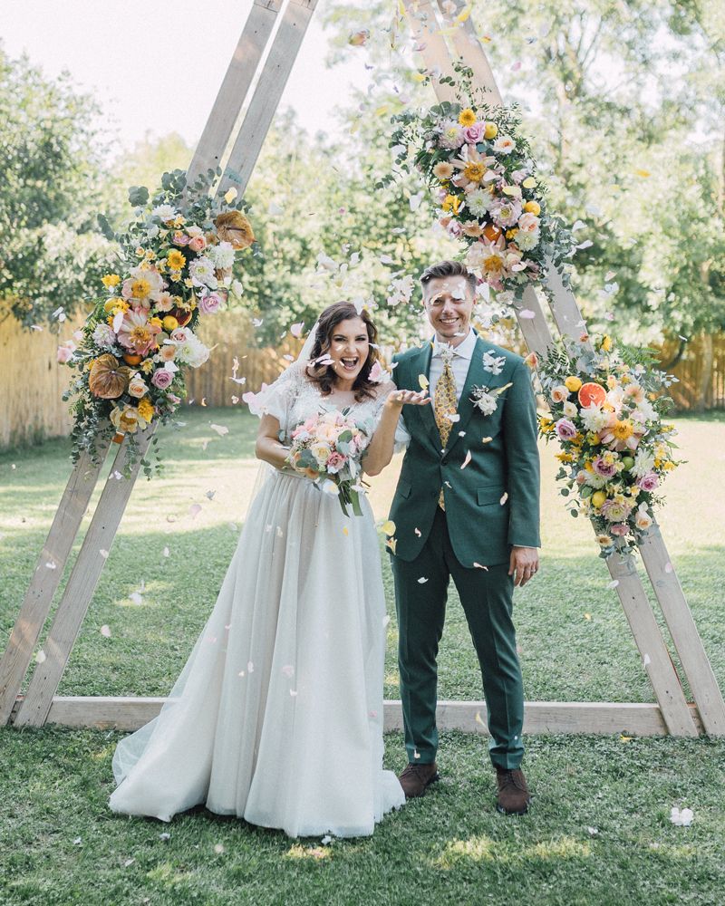 A joyful couple shares a romantic moment outdoors surrounded by lush greenery and colorful floral arrangements.