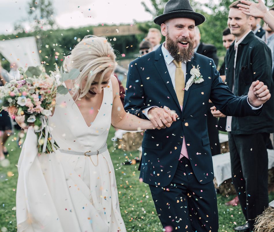 A joyful bride and groom walk through colorful confetti during their outdoor wedding celebration.